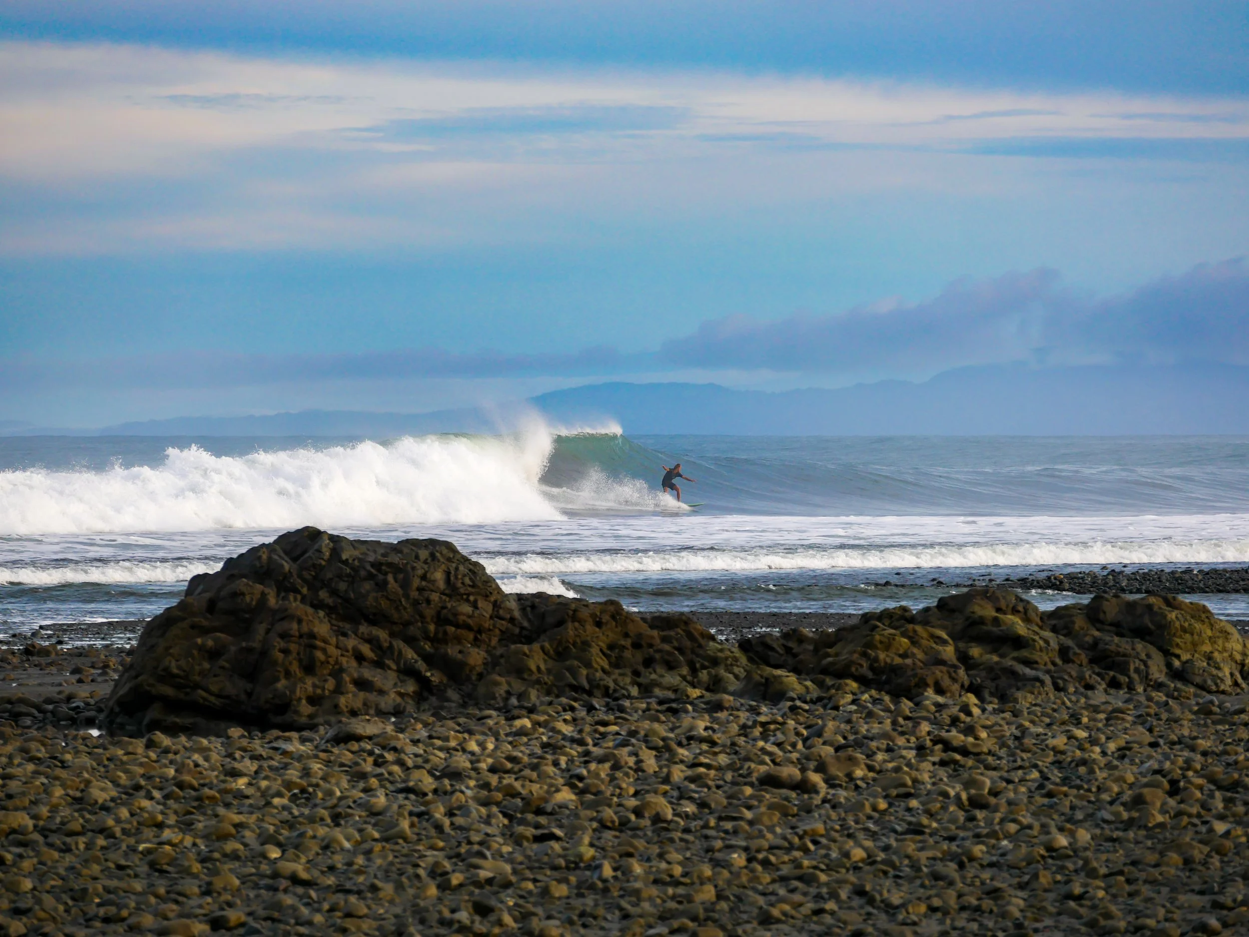 Surfer on a wave at a rocky beach