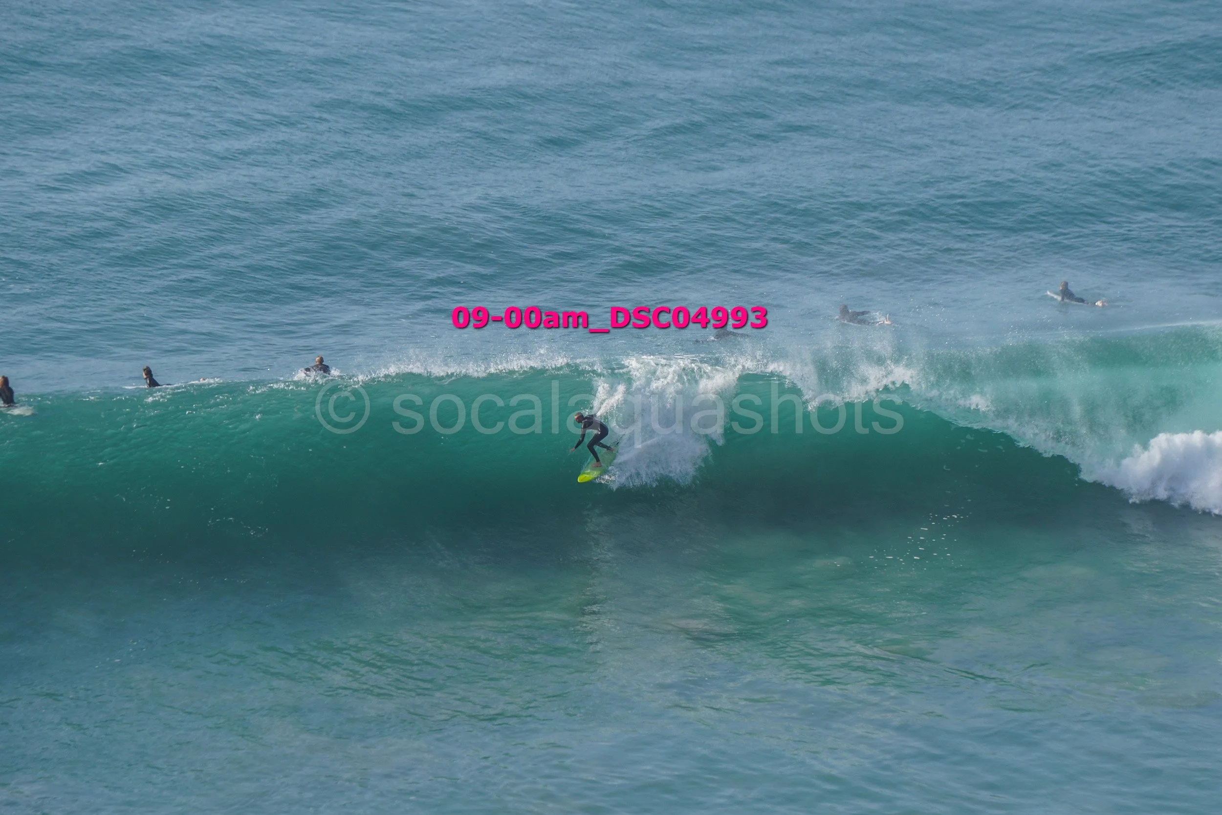 A person in a wetsuit surfing on a wave with other surfers in the background in the ocean.