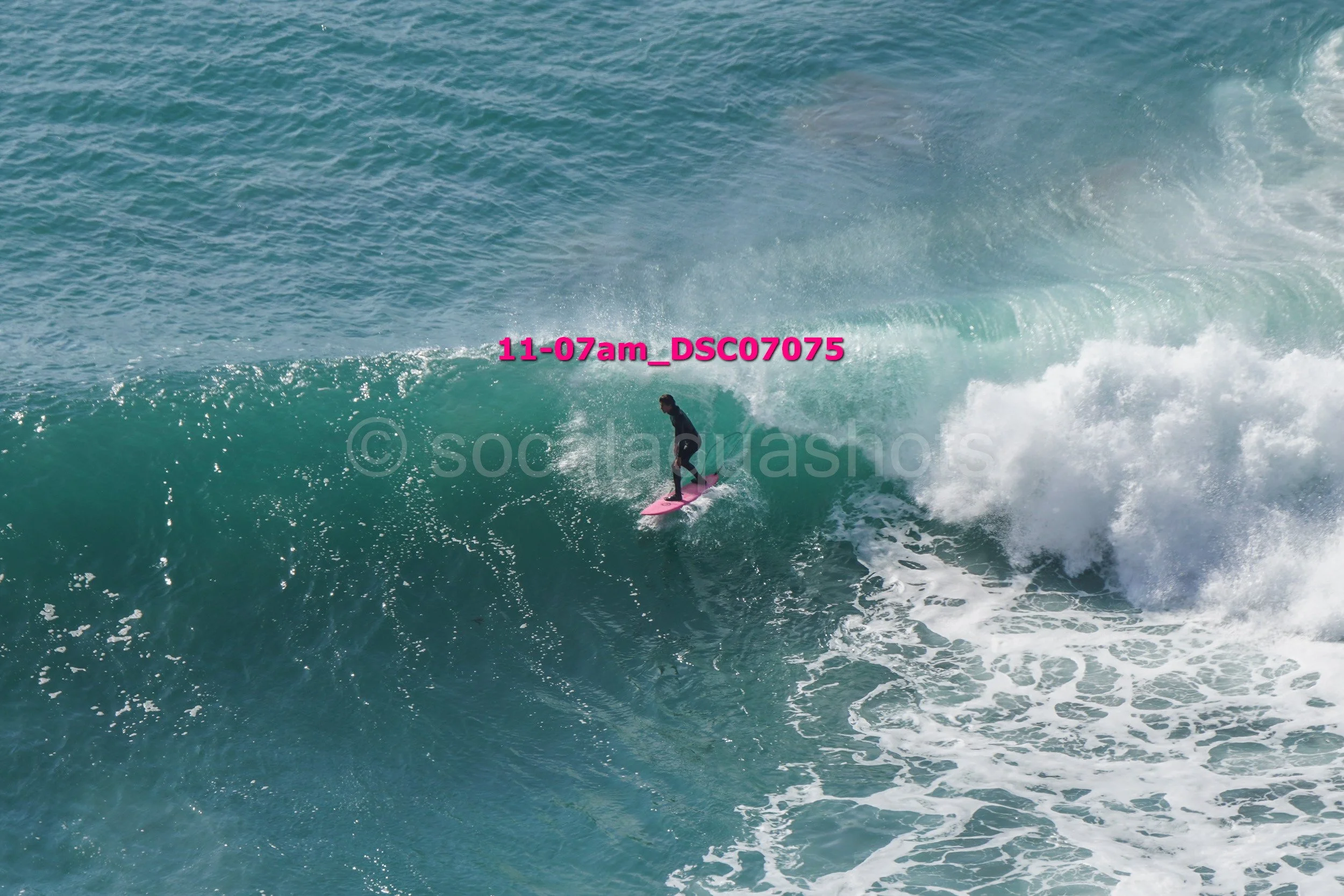 A person surfing on a pink surfboard riding a large wave in the ocean.