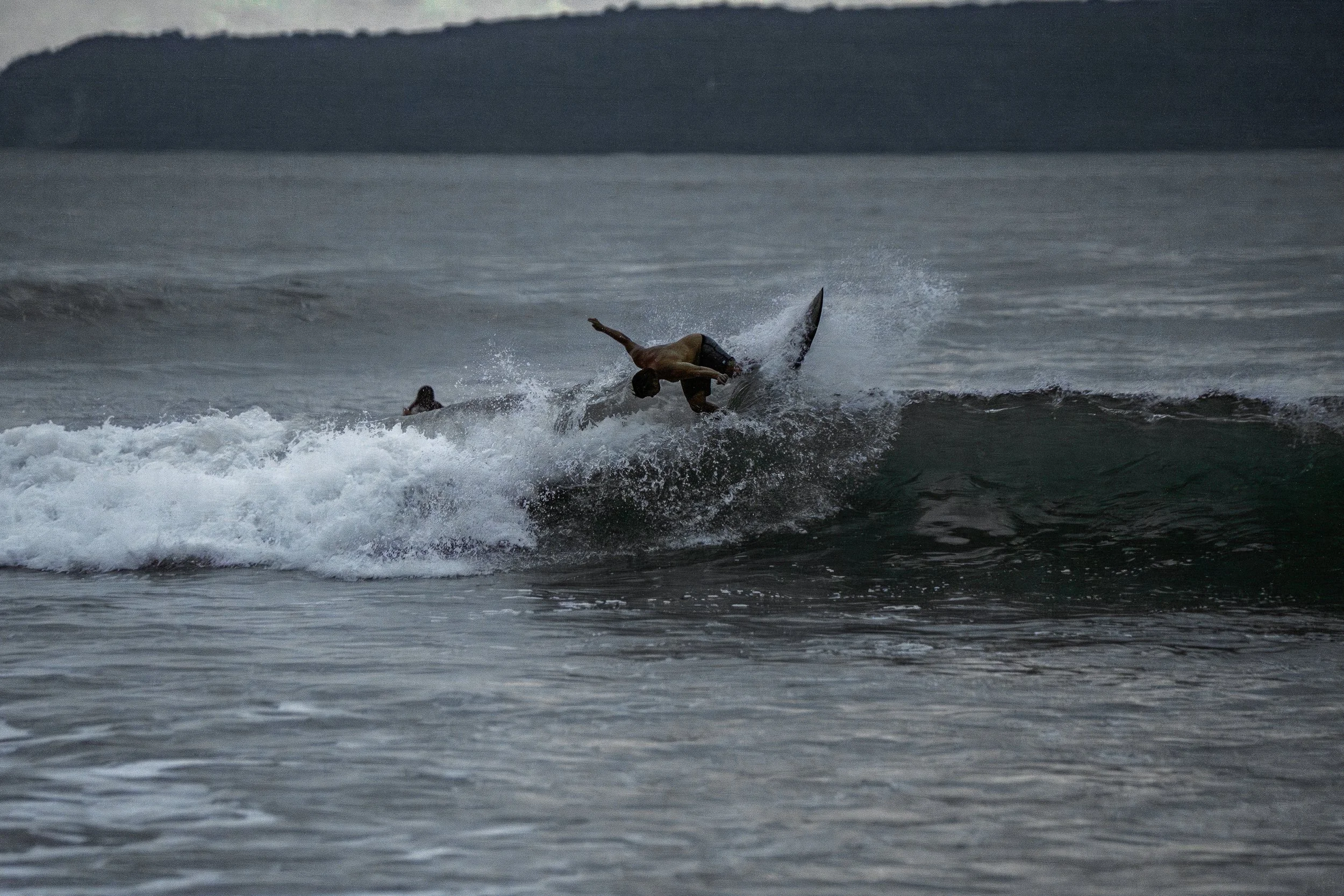 A person surfing on a wave in the ocean during twilight.