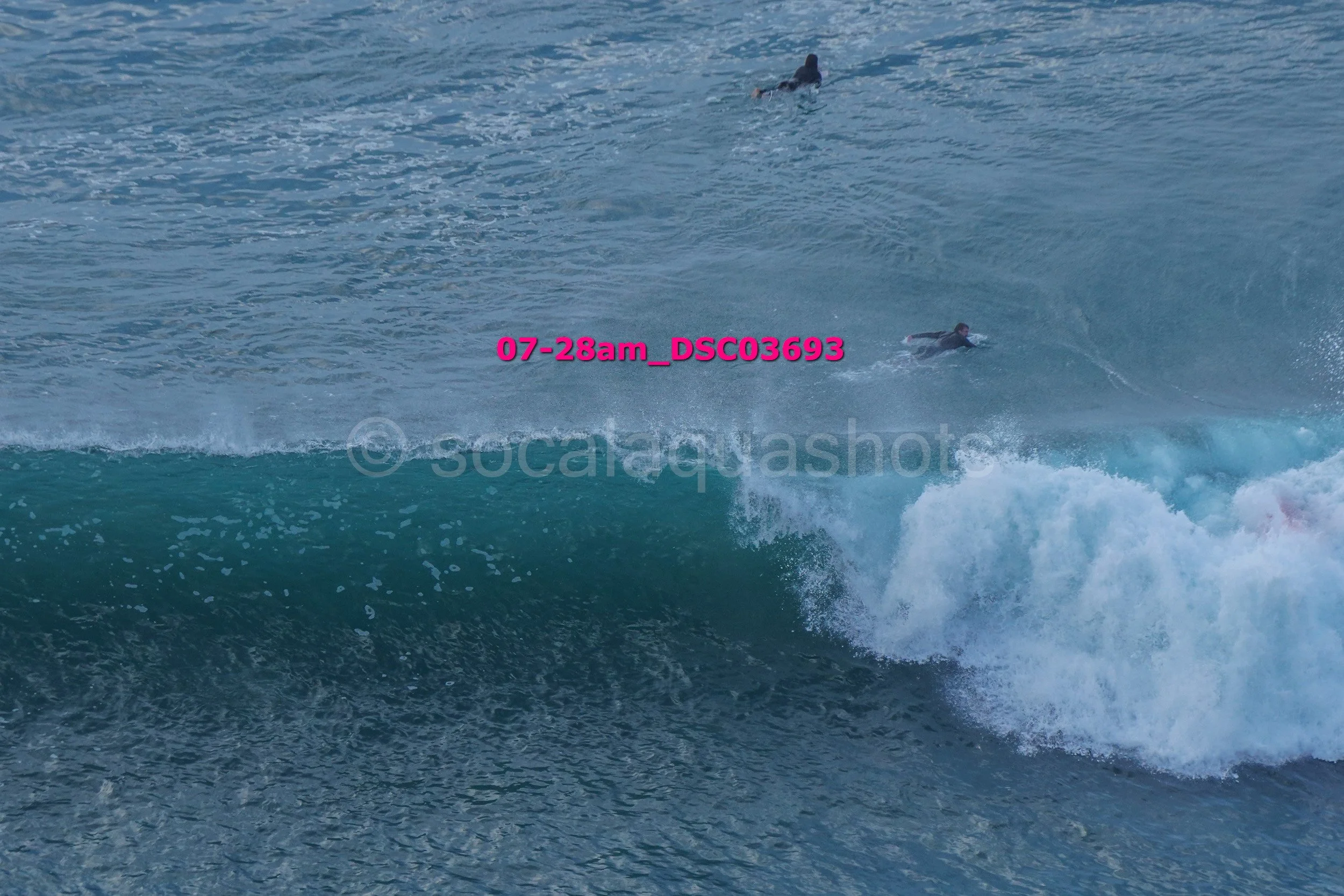 Two surfers riding a wave in the ocean, with one surfer visible in the distance and the other closer to the camera.