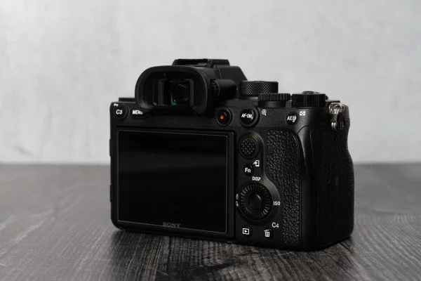 A black Sony mirrorless camera with a viewfinder, LCD screen, and various control buttons, placed on a dark wooden surface.