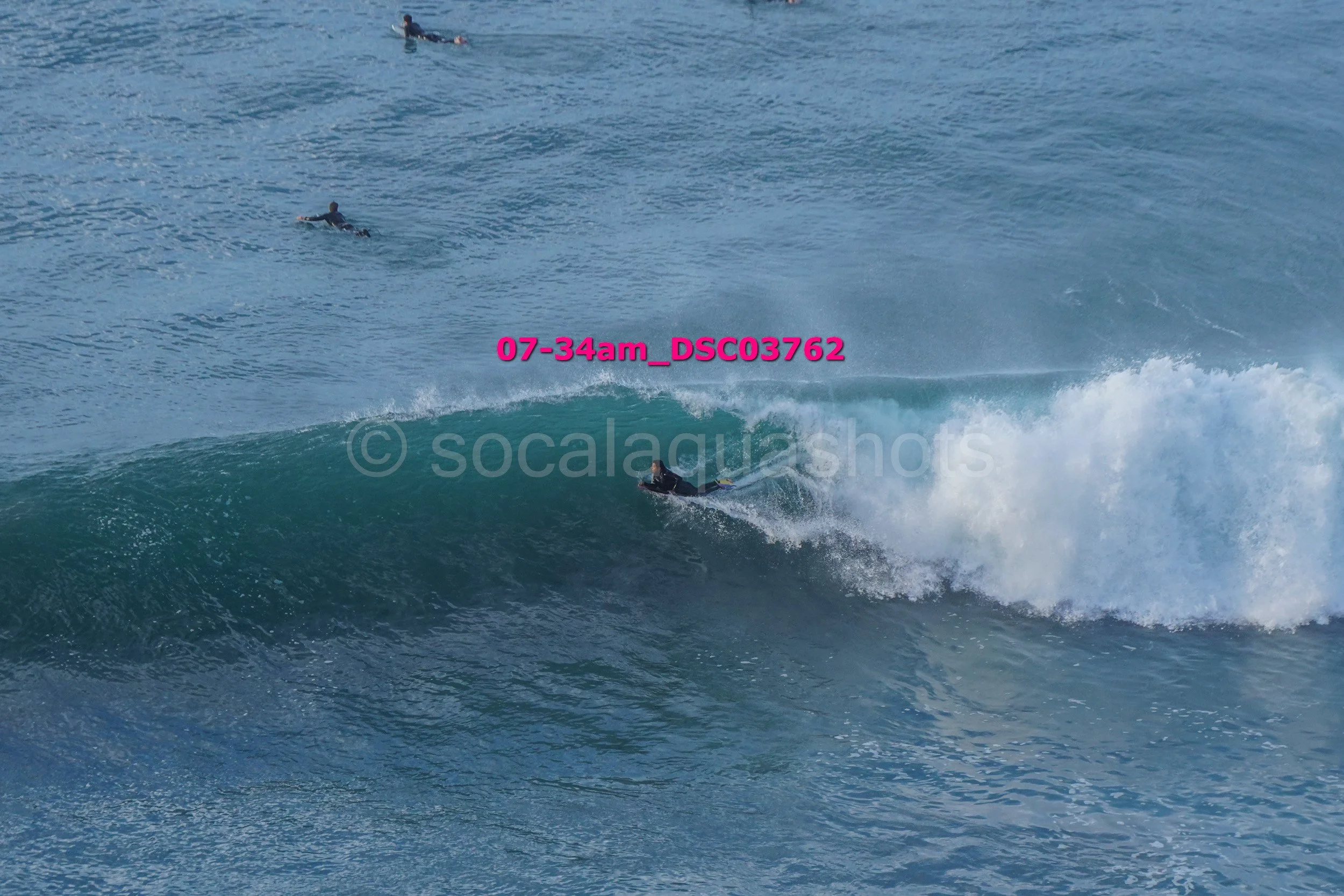 Surfer riding a wave with two others in the water nearby in the ocean.
