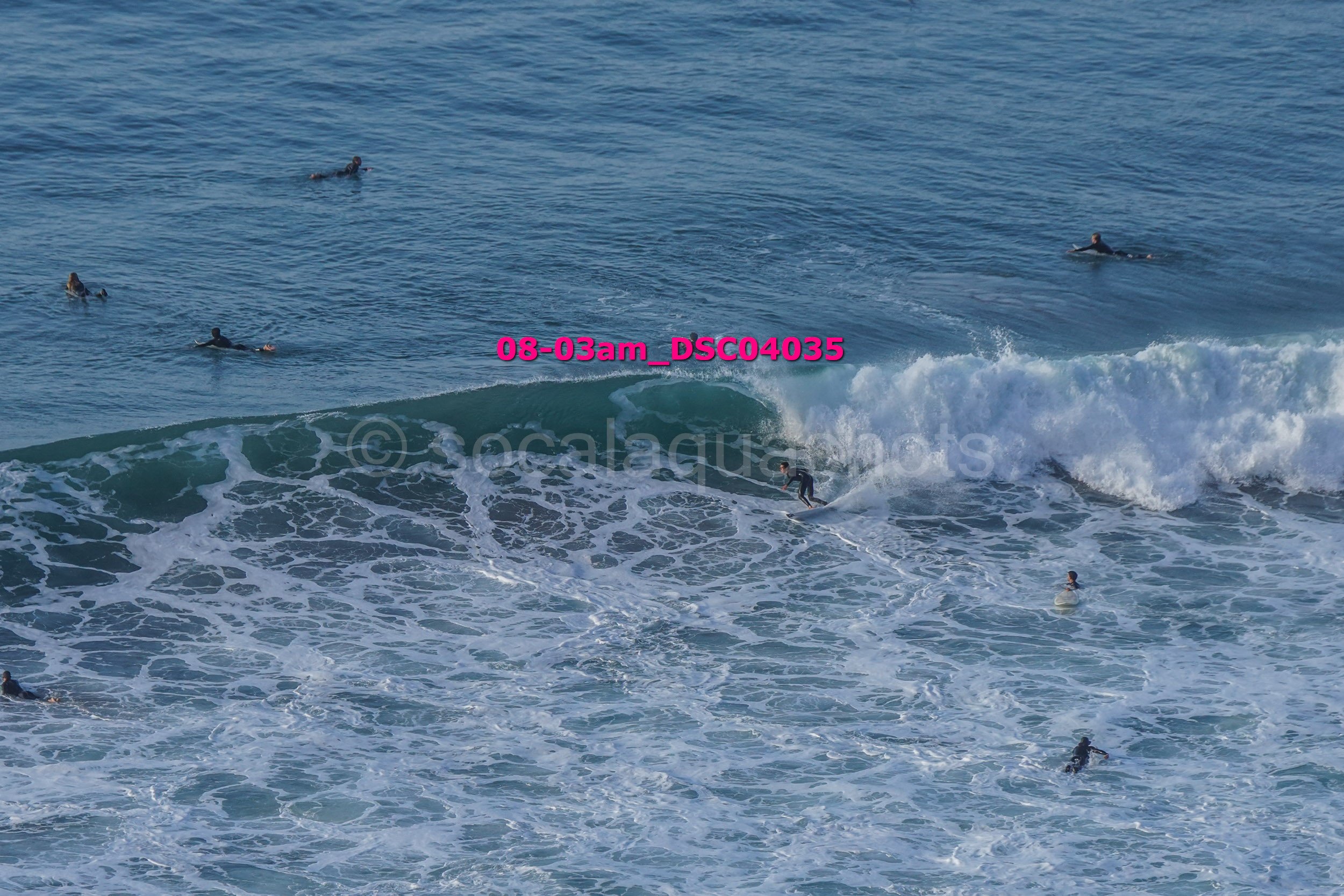 Surfers in the ocean, some riding waves and others swimming or waiting in the water.