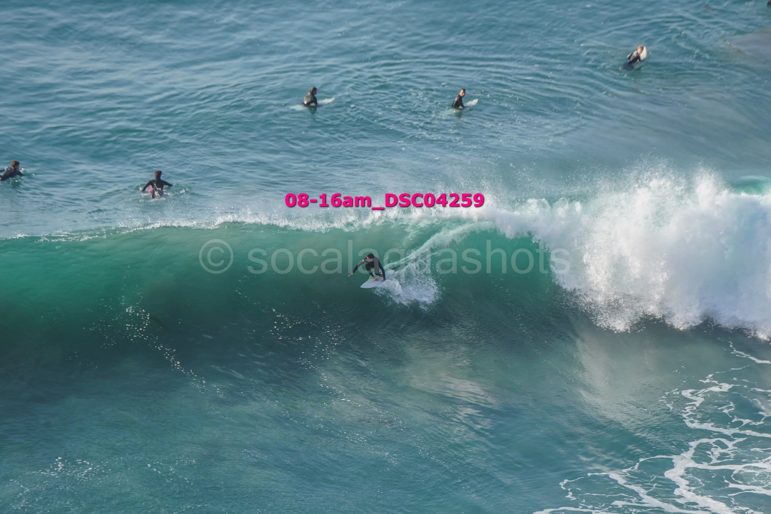 Surfer riding a wave with multiple surfers in the water nearby.