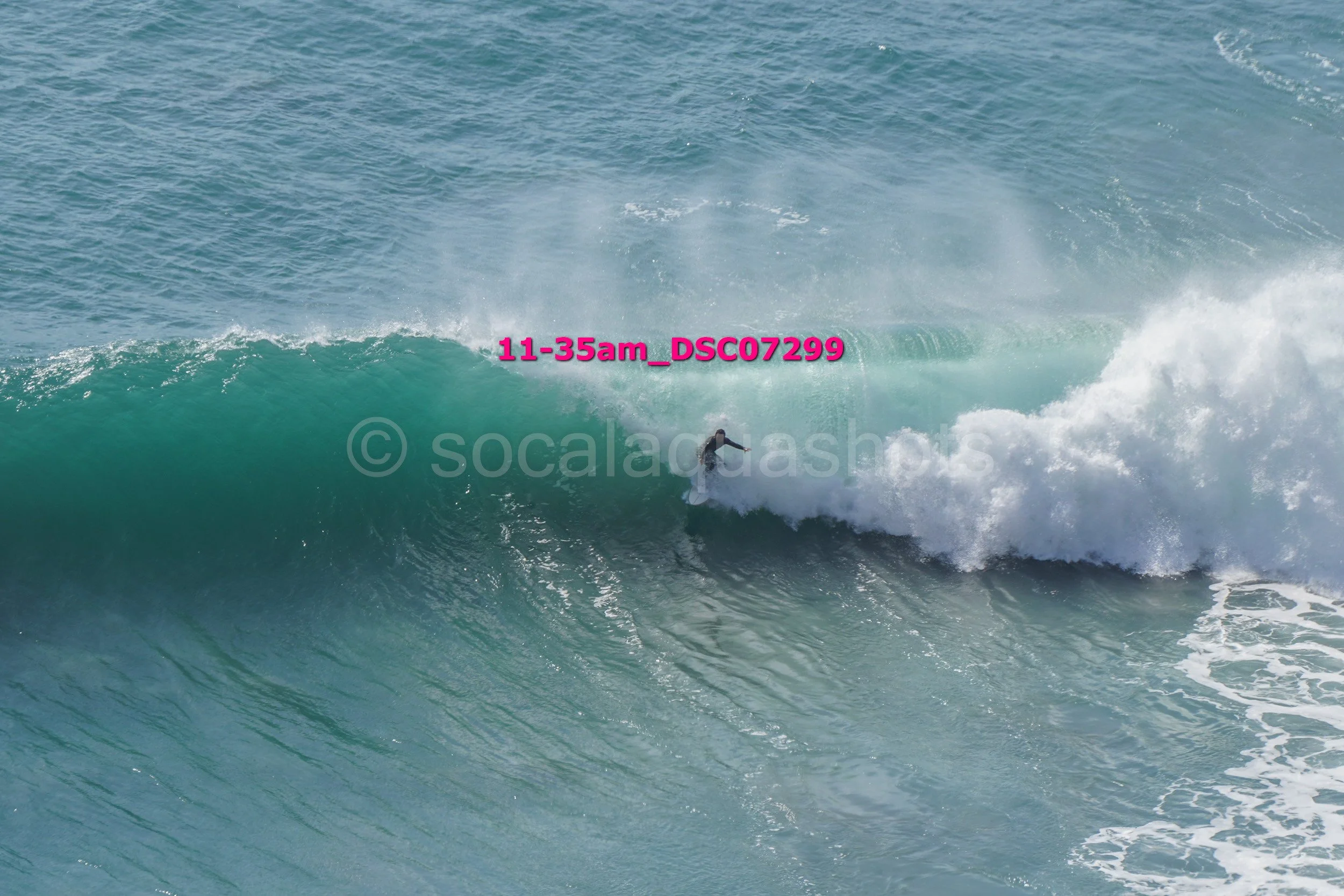 A surfer riding inside a large ocean wave with white foam at the front, water spraying at the top, and the ocean stretching in the background.