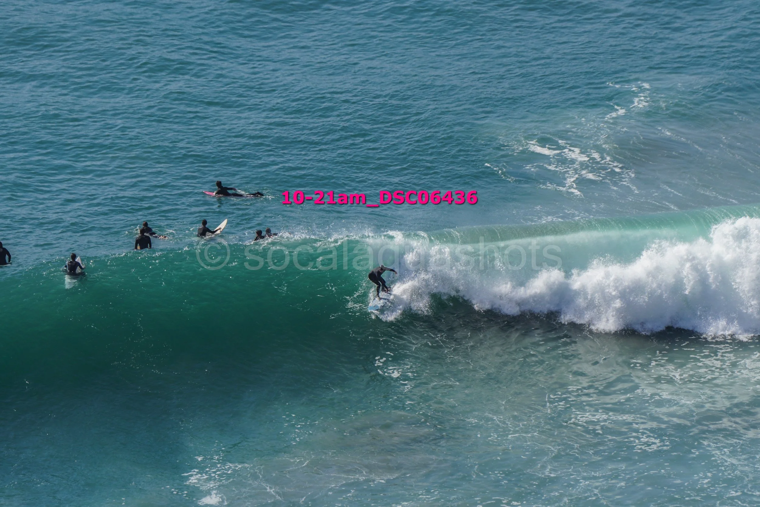 Surfer riding a wave with several other surfers in the water nearby.