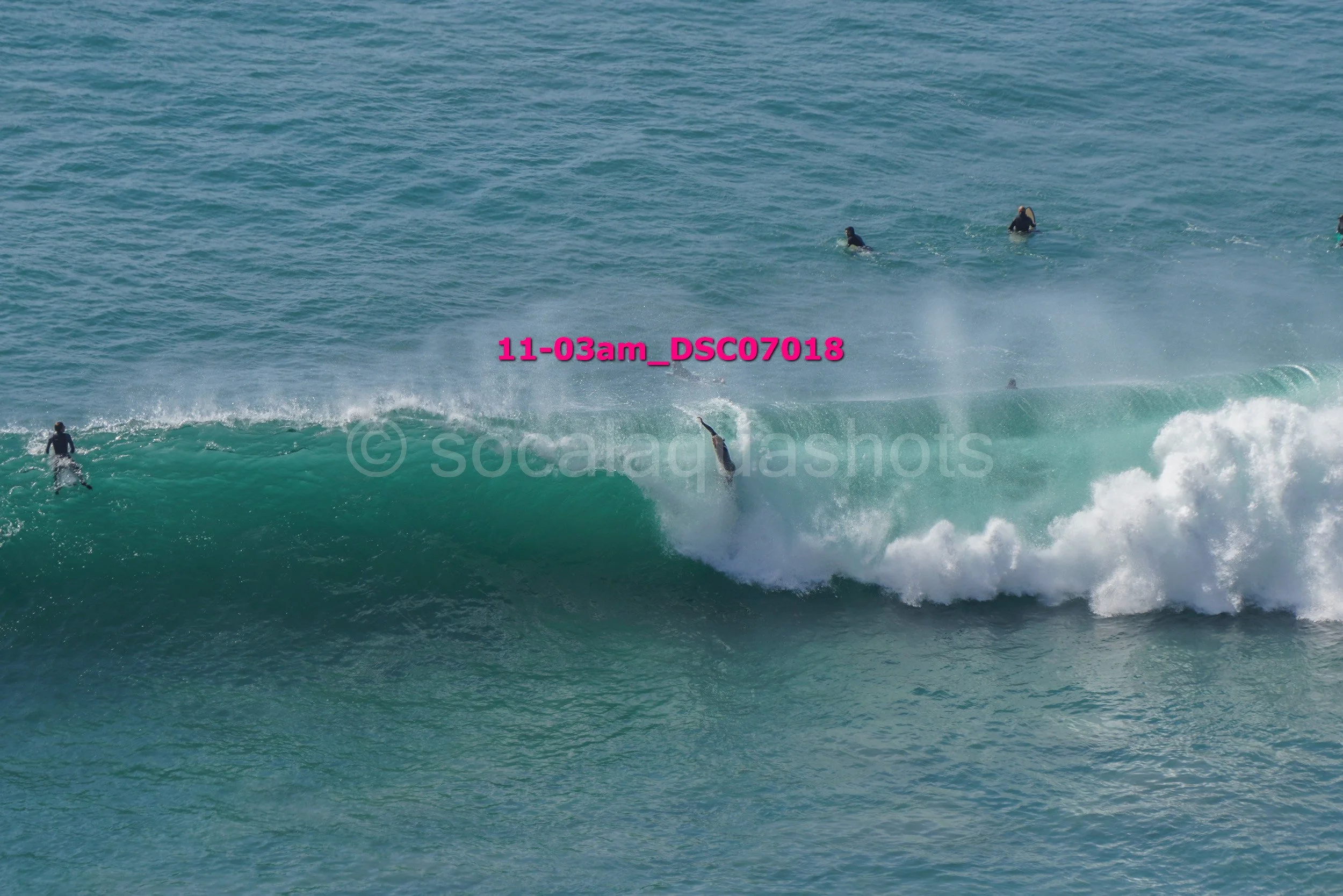 Surfer falling off their surfboard on a wave with a few other surfers in the water in the background.