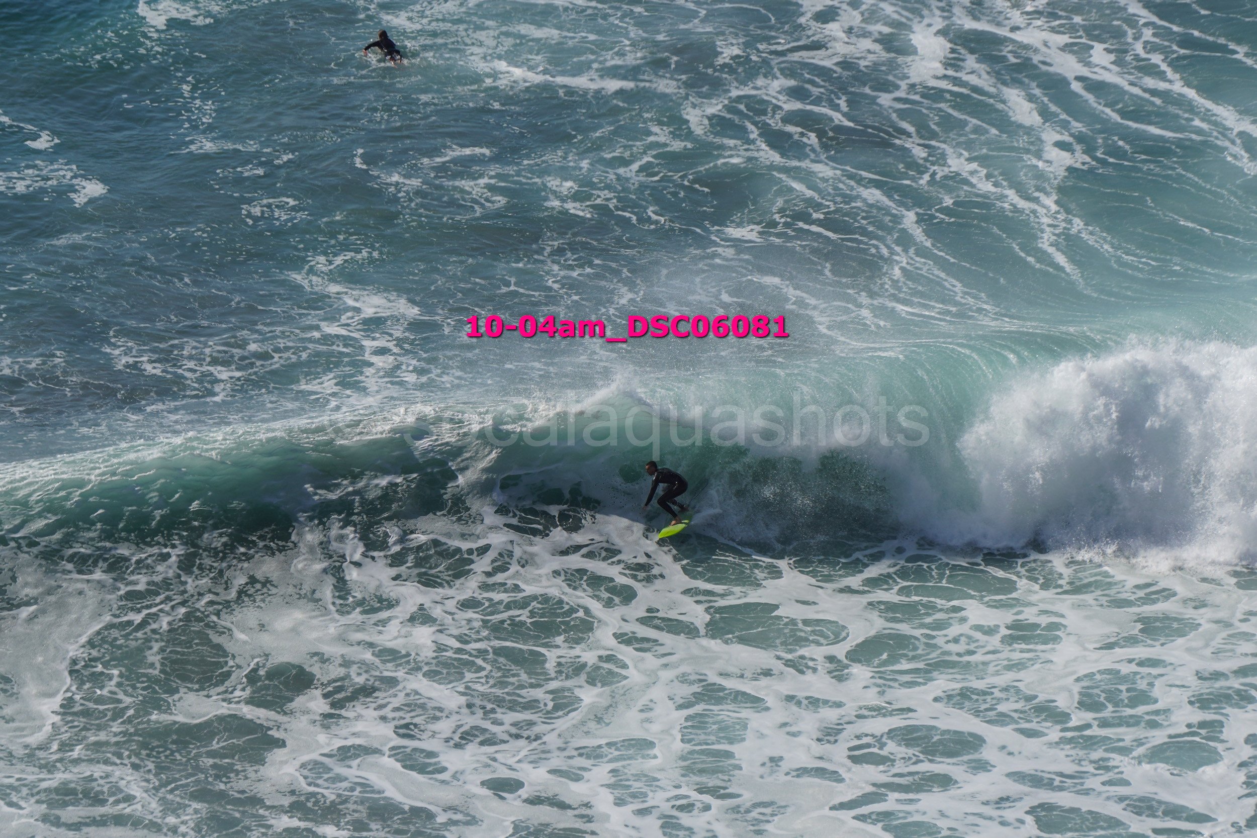 A person surfing on a small wave in the ocean, with another surfer visible in the distance.