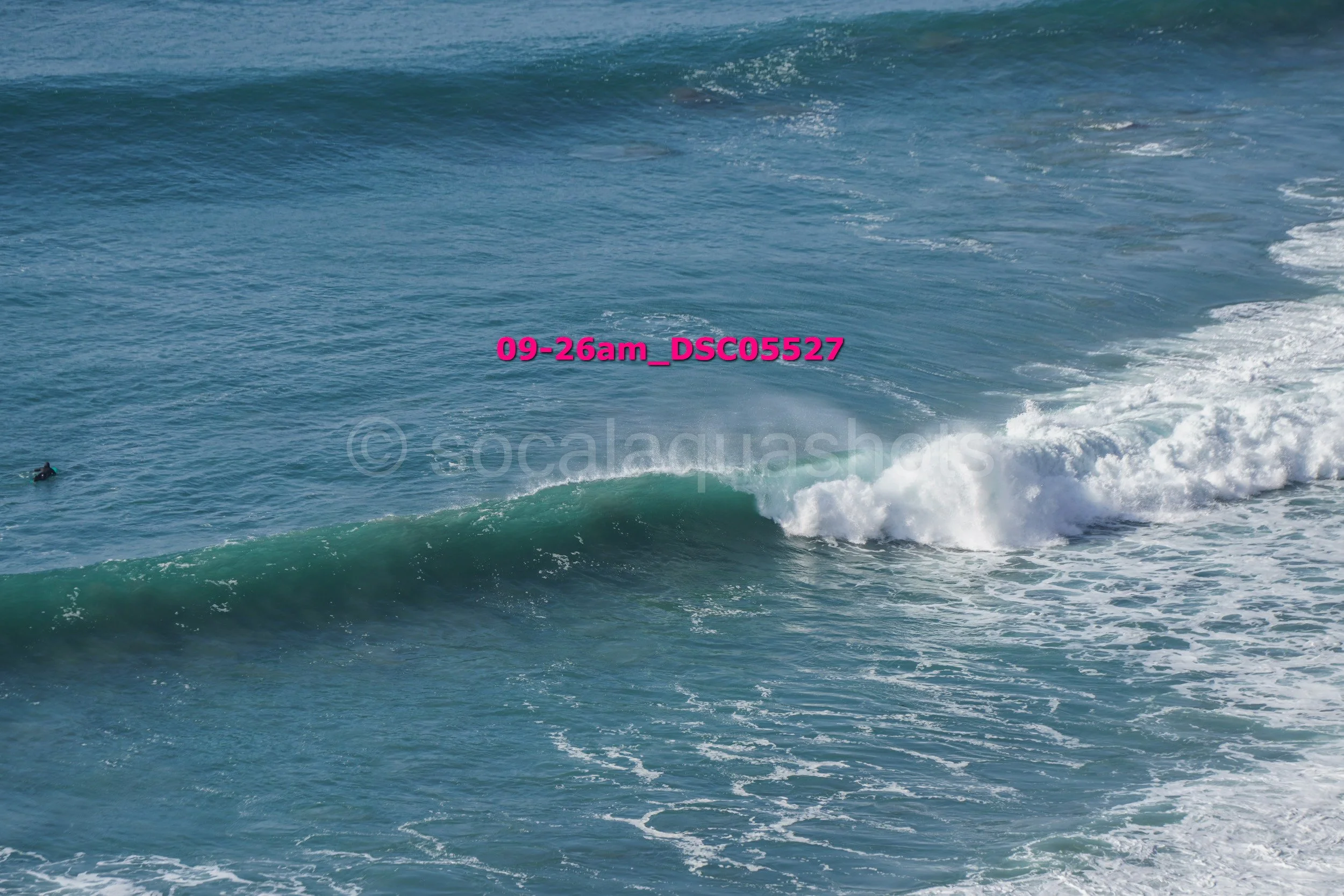 Ocean waves with a surfer in the water and a watermark that reads "09-26am_DSC05527"