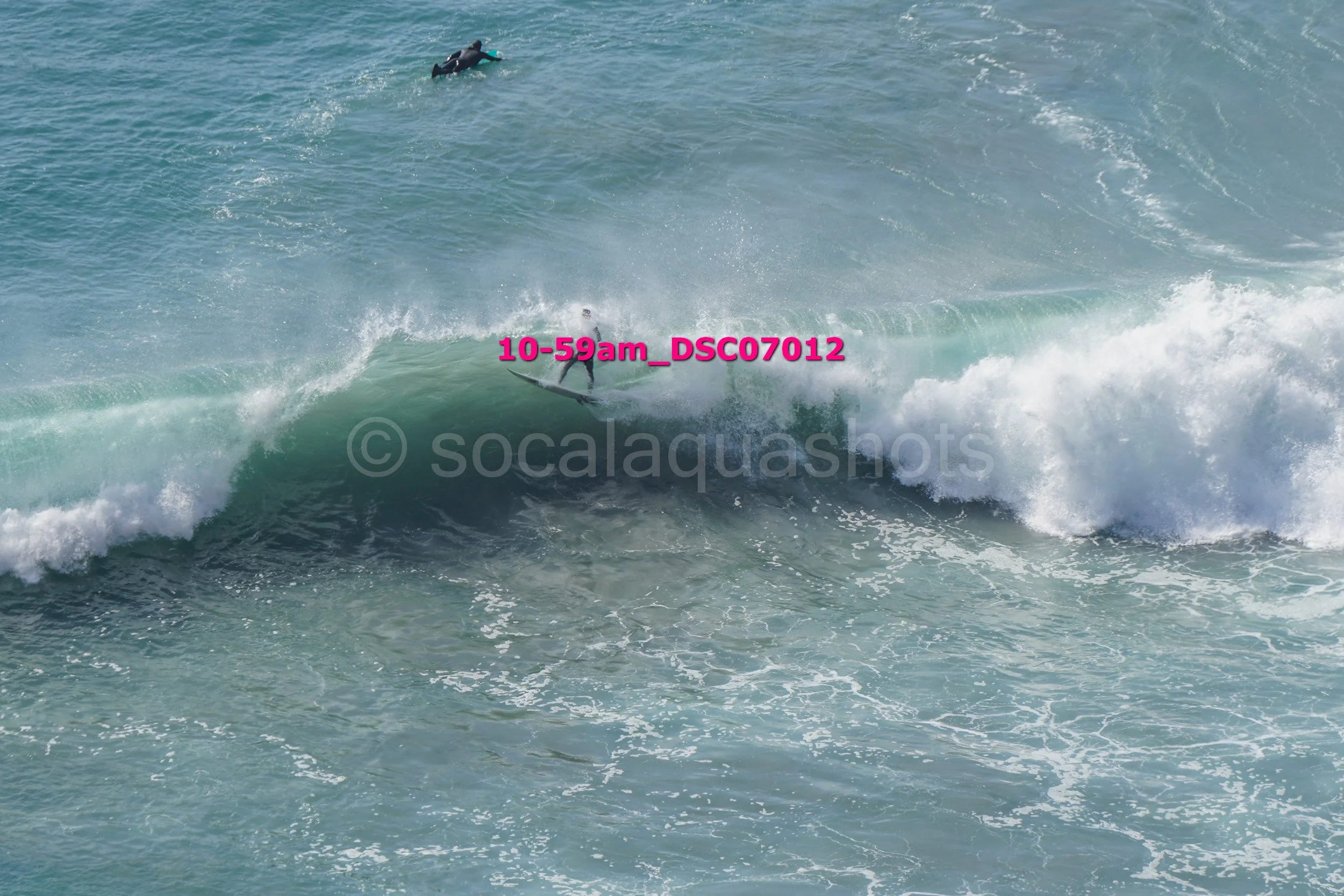 A person surfing on a wave in the ocean with another surfer in the background.
