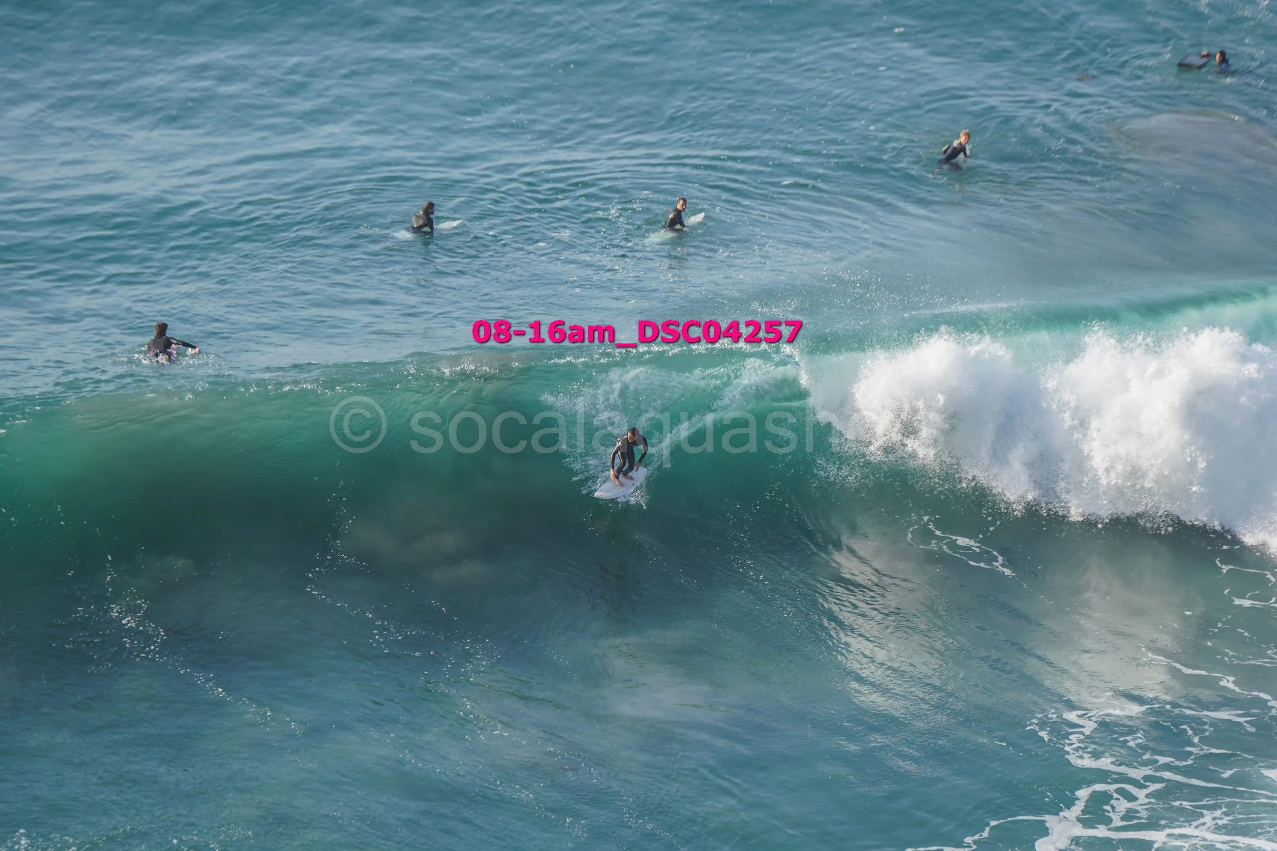 A person surfing on a large wave with several other surfers in the water nearby.