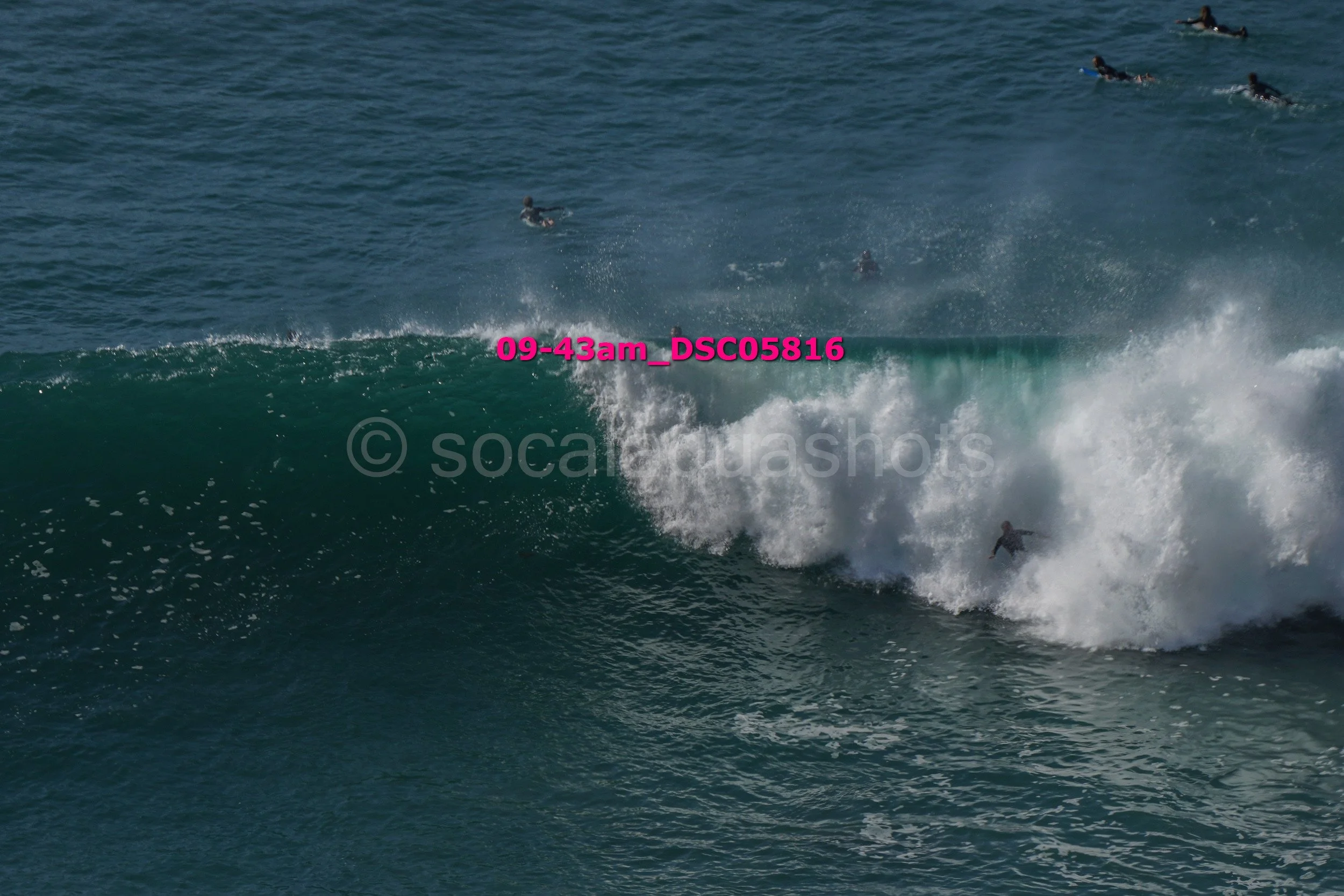 Surfer riding a large wave with other surfers in the water in the background.