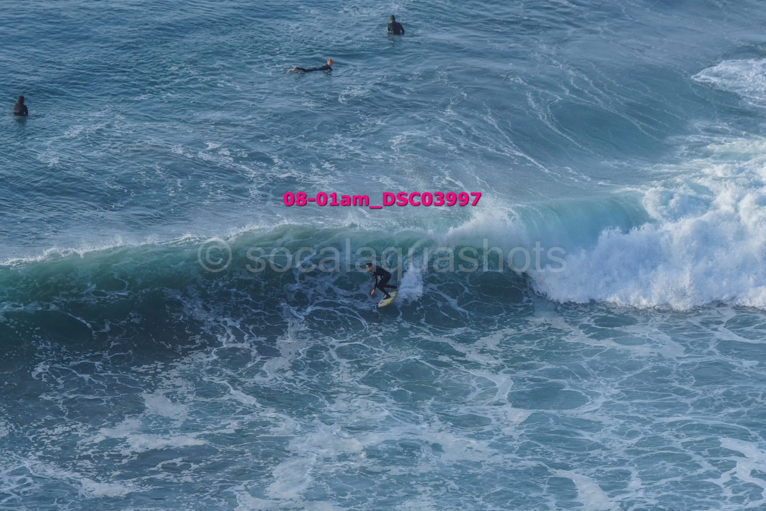 Surfer riding a wave with three other surfers visible in the water nearby.