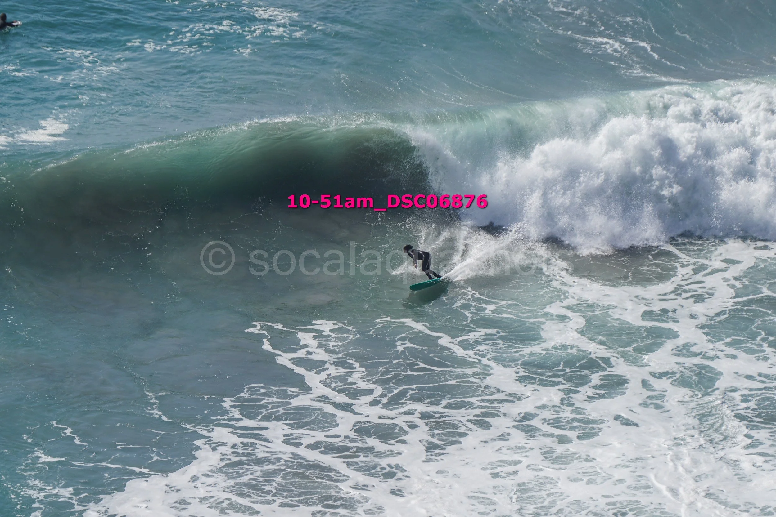 A person surfing on a wave in the ocean, wearing a wetsuit and riding a surfboard, with the text '10-51am_DSC6876' overlaid in pink.