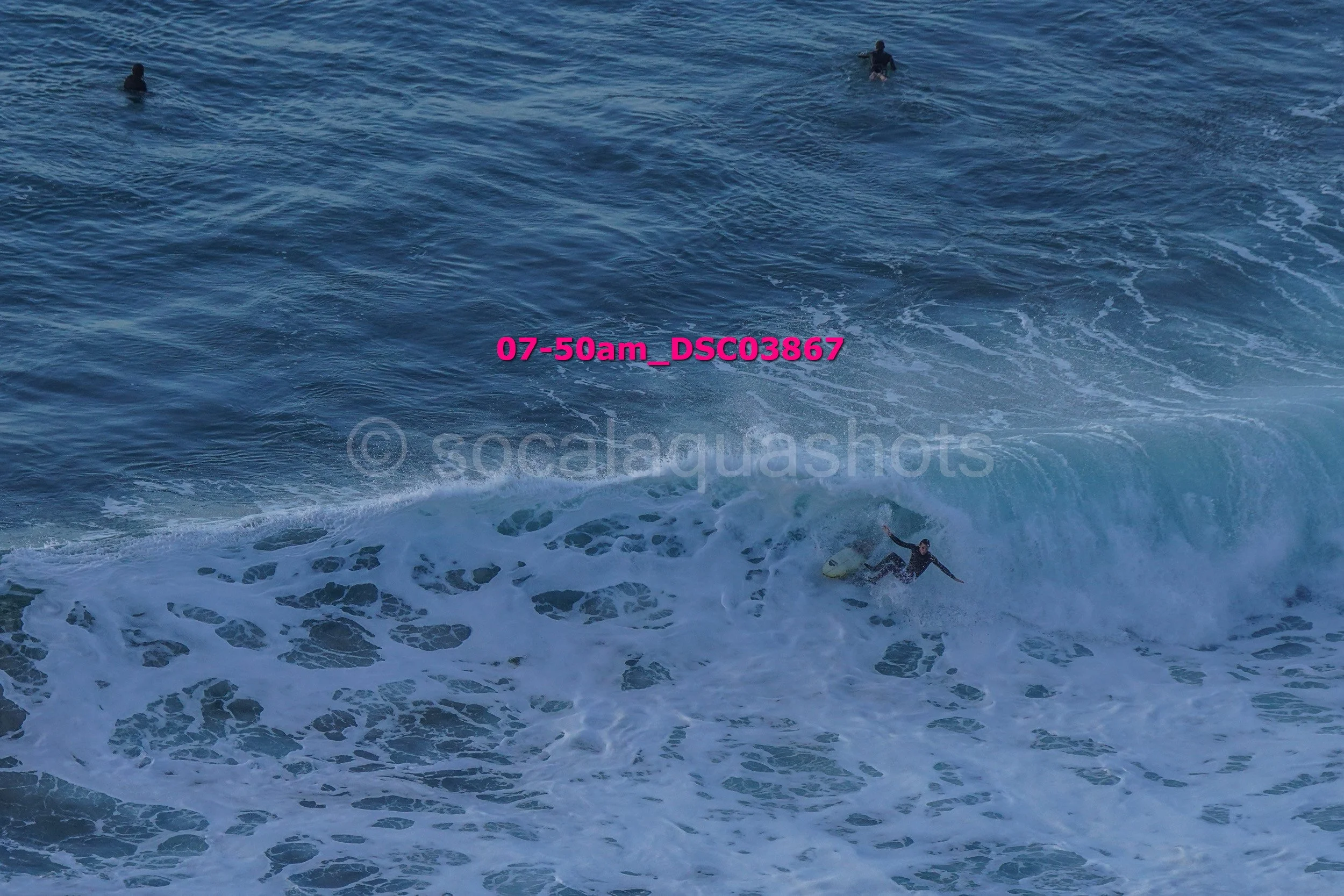 A surfer riding a wave in the ocean, with two other people swimming in the background.