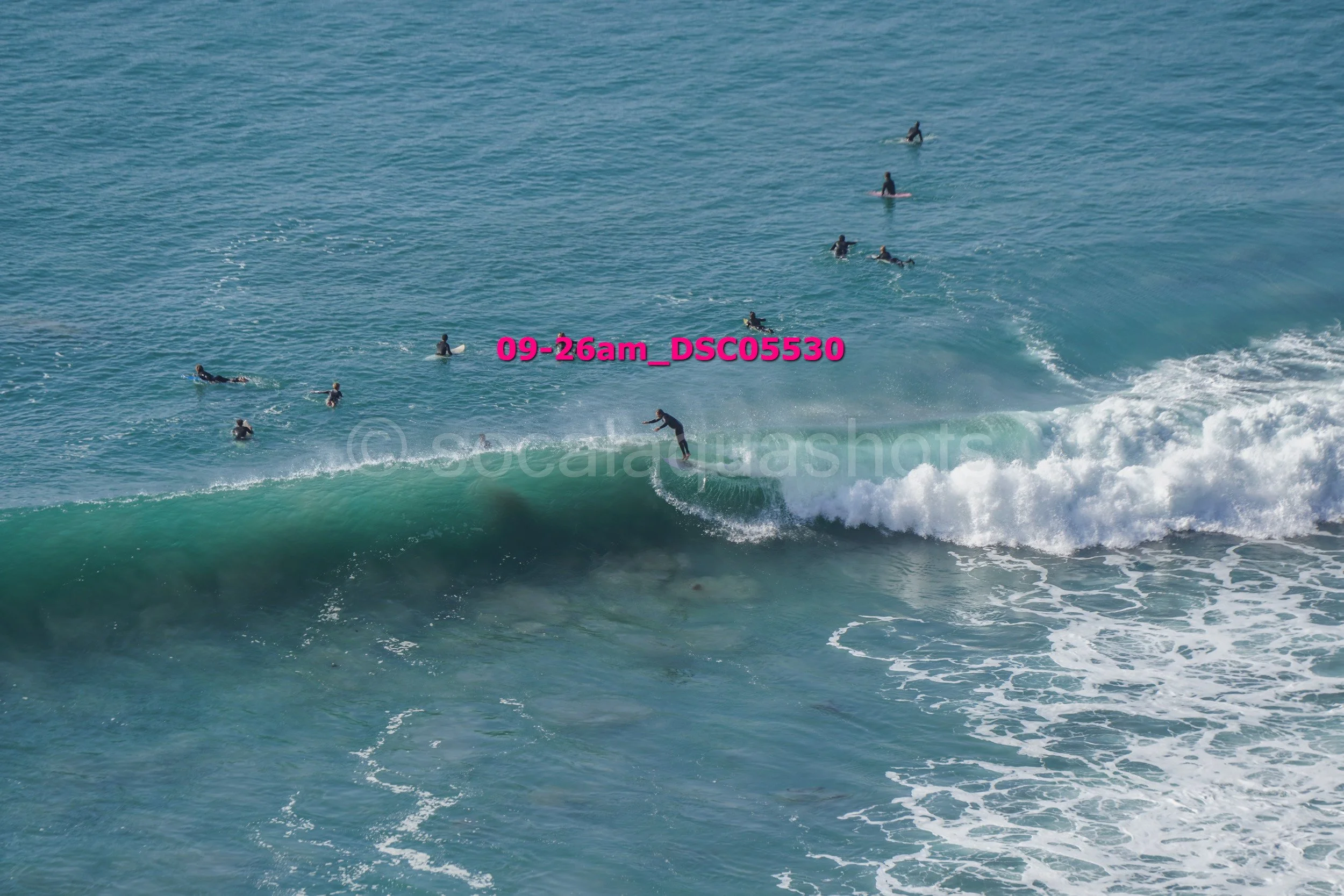 Surfer riding a wave with several surfers in the water behind him.