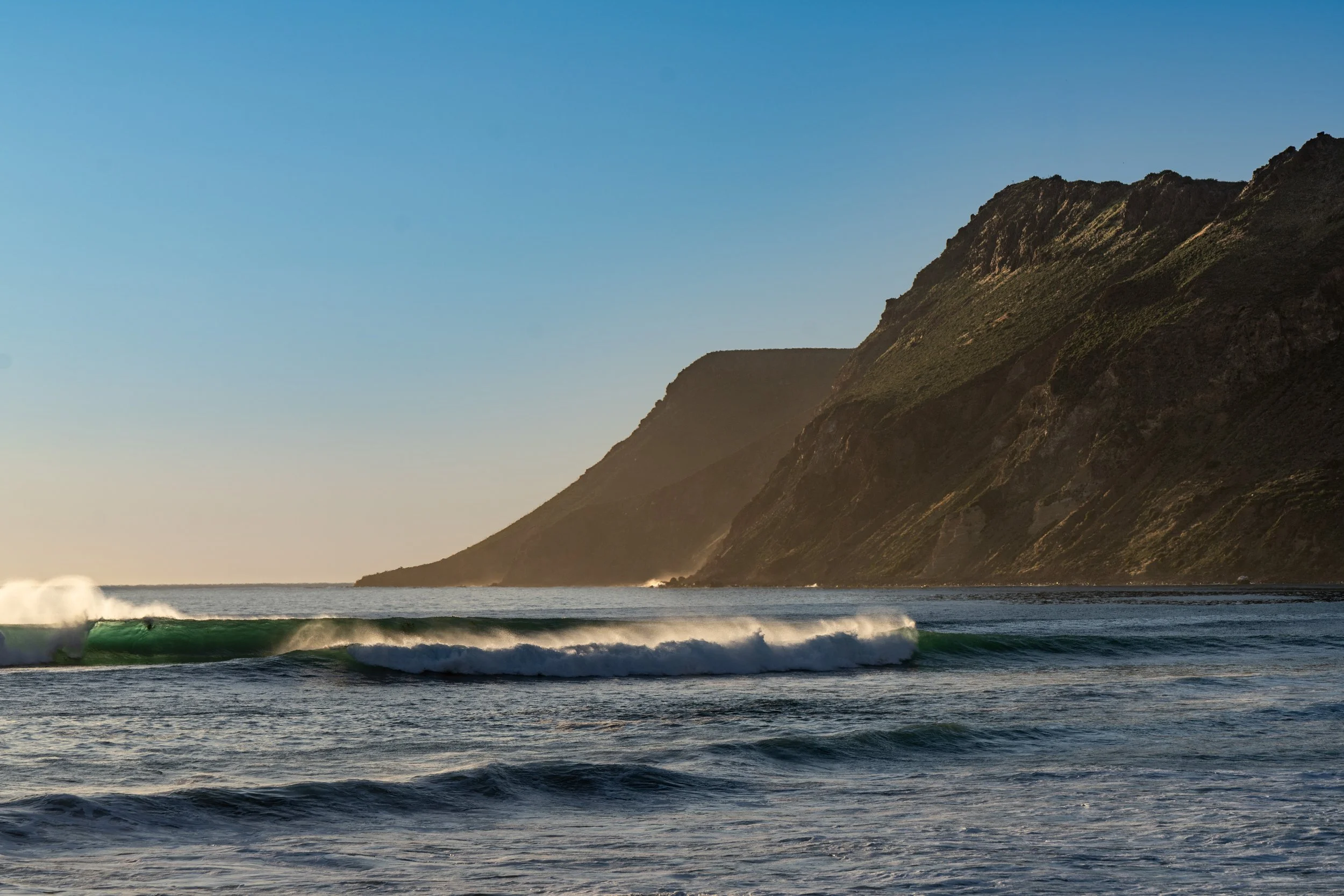 Ocean waves crashing near a mountainous coastline at sunset