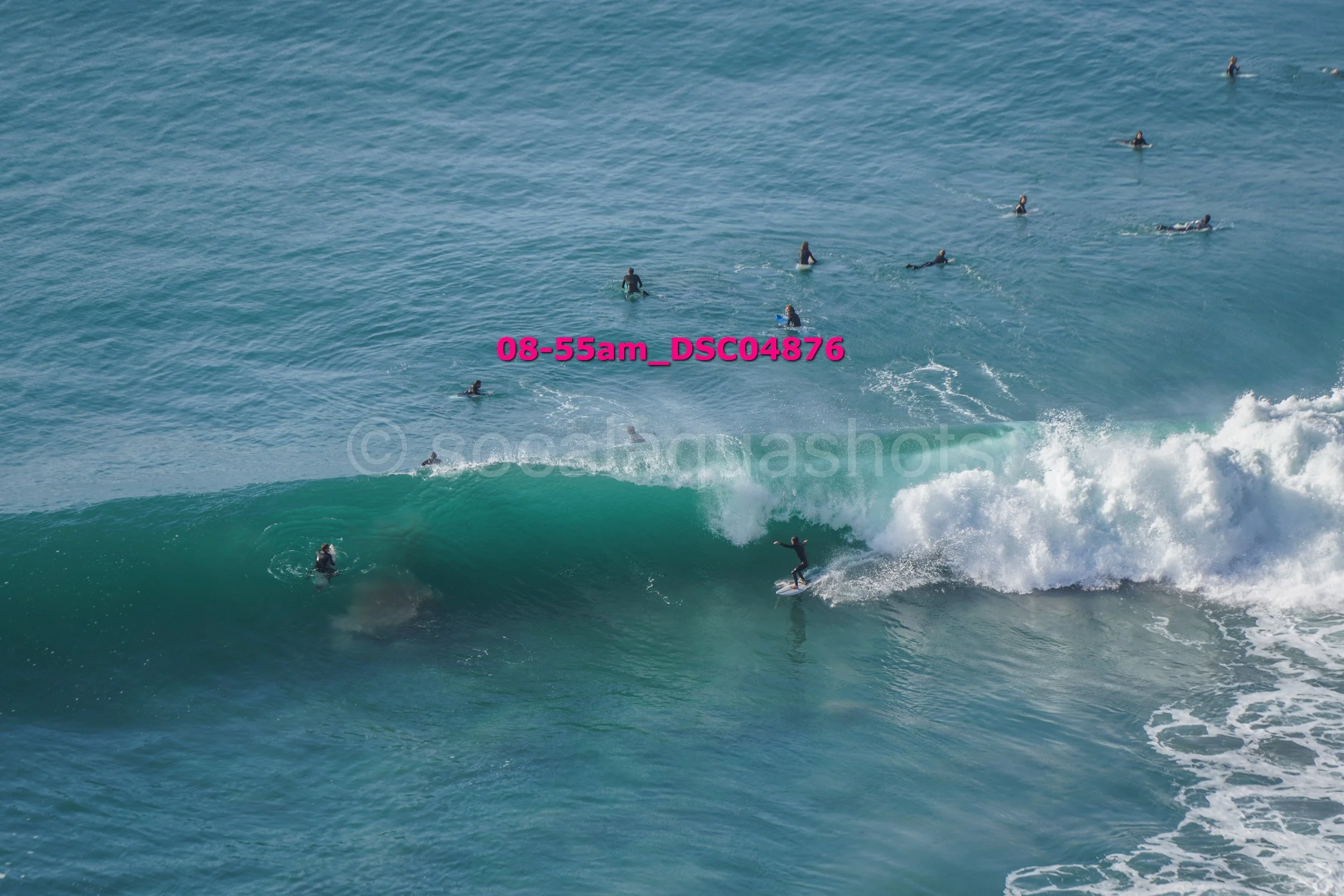 Surfer riding a wave with multiple surfers in the water and others in the distance.