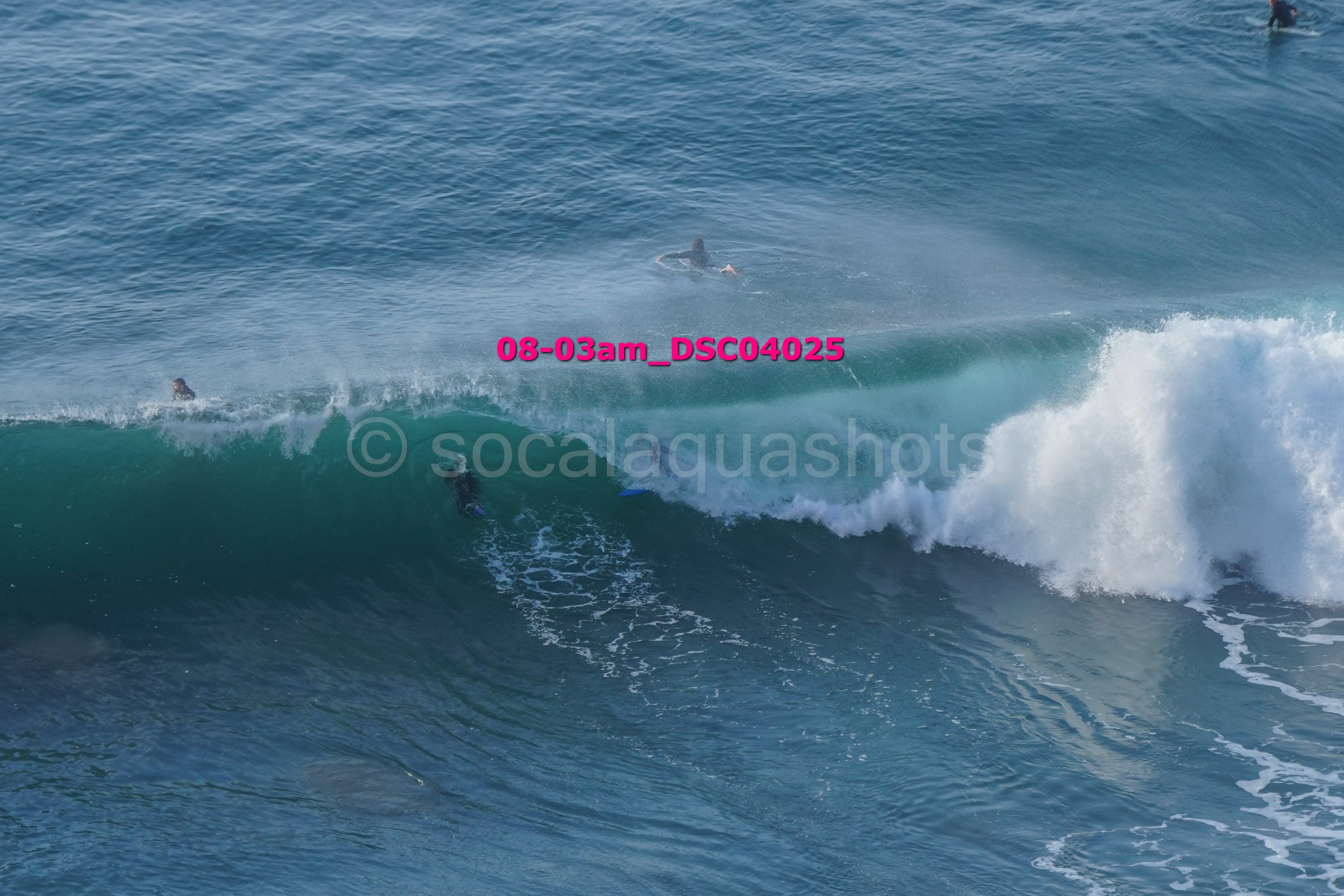 Surfers riding ocean waves with one surfer visible on a board in the water, and two others further back in the ocean.