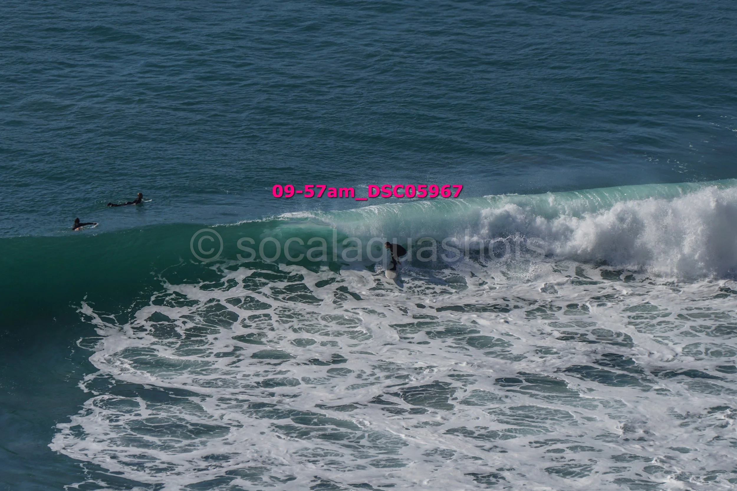 Surfers in the ocean riding a wave and waiting for their turn, with one surfer riding a wave.