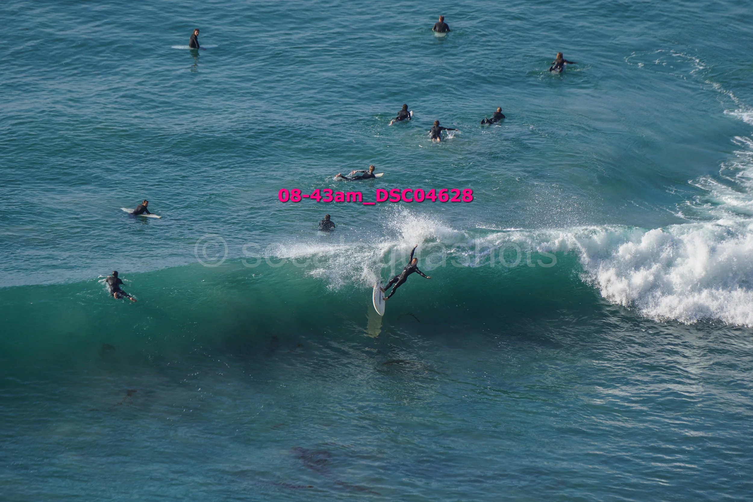 Surfer performing a trick on a wave while multiple people watch in the water.