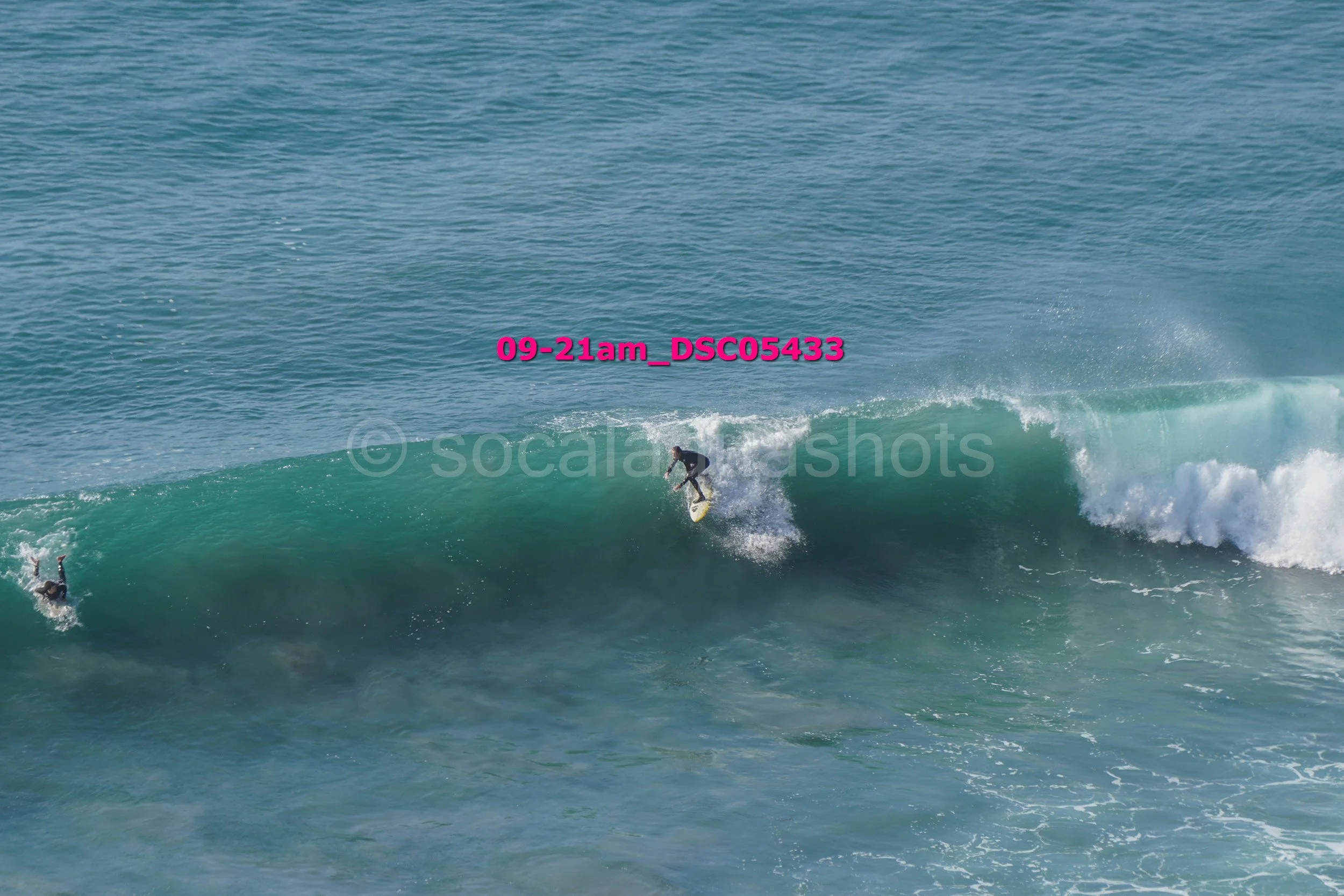 A person surfing on a wave in the ocean, with another person swimming nearby.