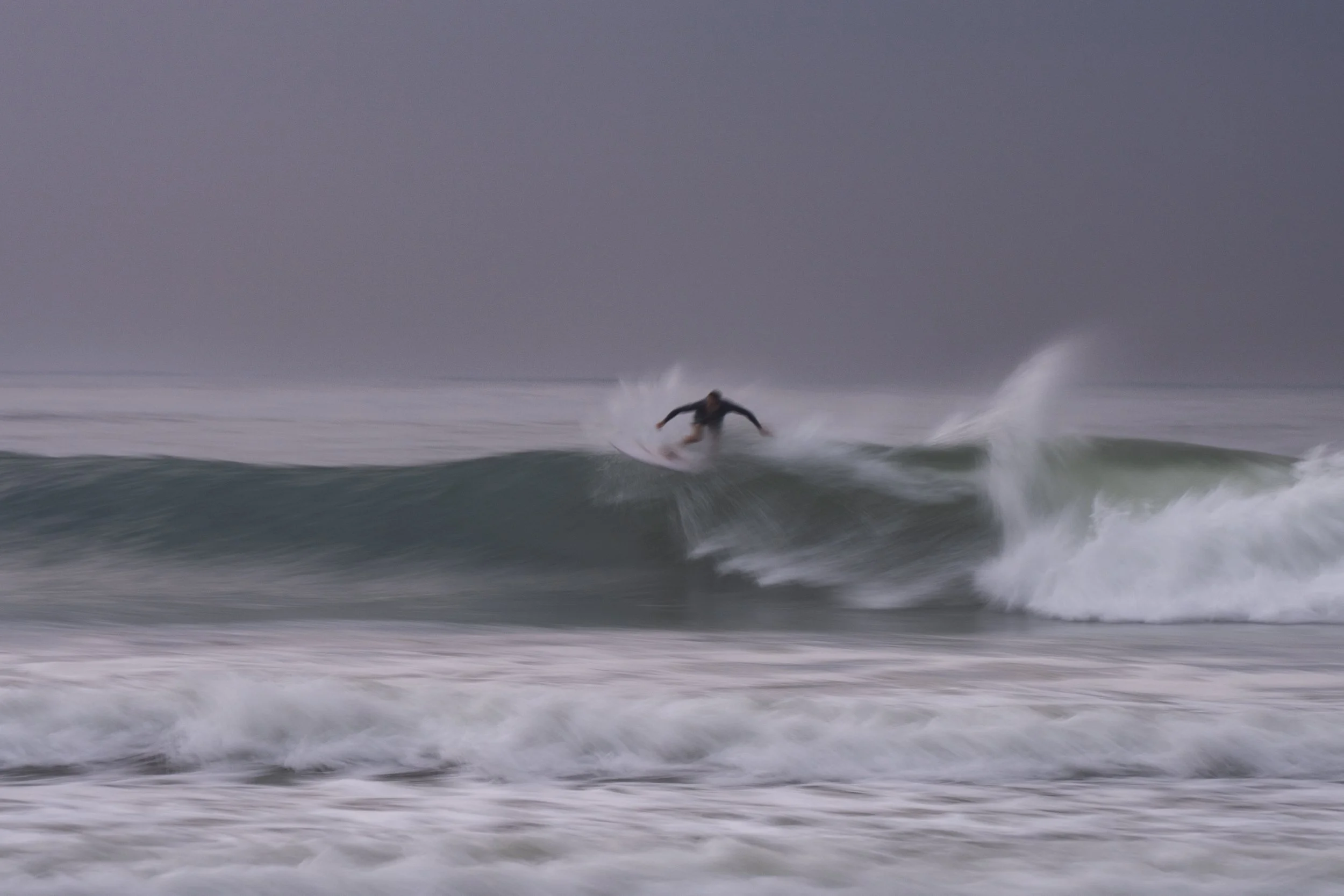 A person surfing on a wave in a stormy ocean under a dark, cloudy sky.