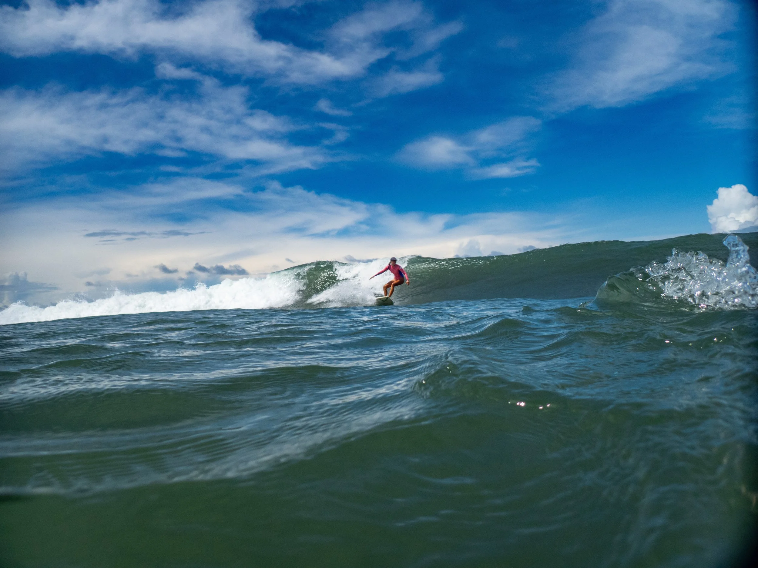 A person surfing on a wave in the ocean with a partly cloudy sky.