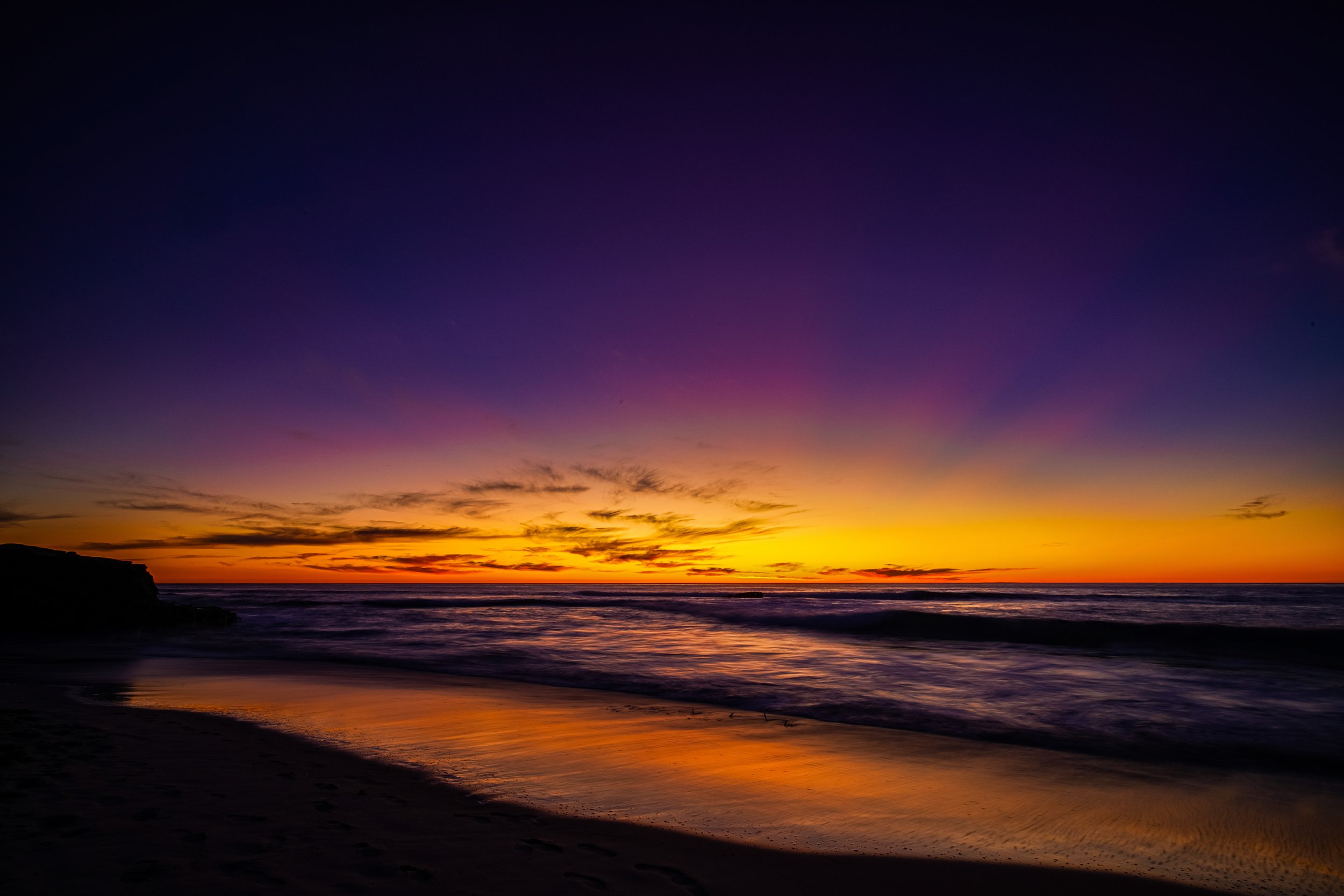 Sunset over the ocean with colorful sky in shades of purple, orange, and yellow, and reflections on wet sand.