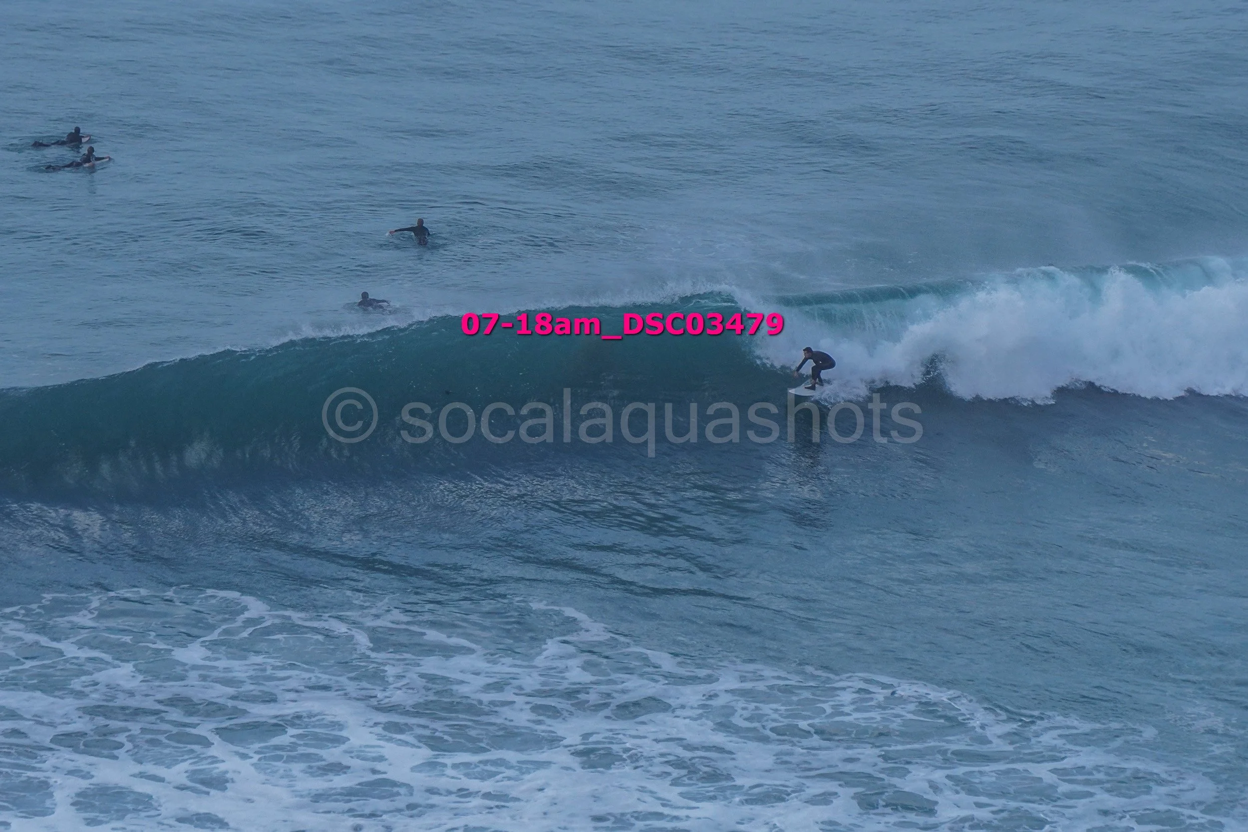 A surfer riding a wave at the beach with several other surfers in the water in the background.