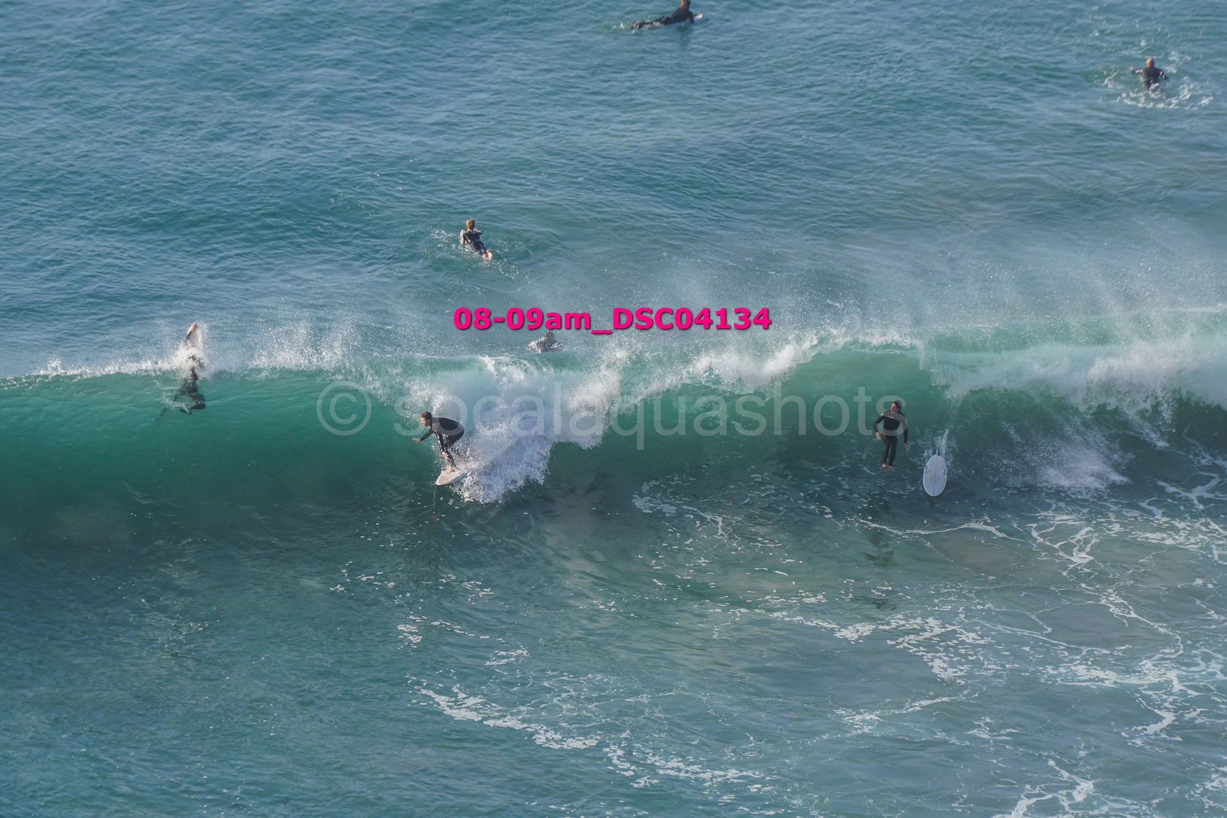 Multiple surfers riding and paddling on large ocean waves in sunny weather.
