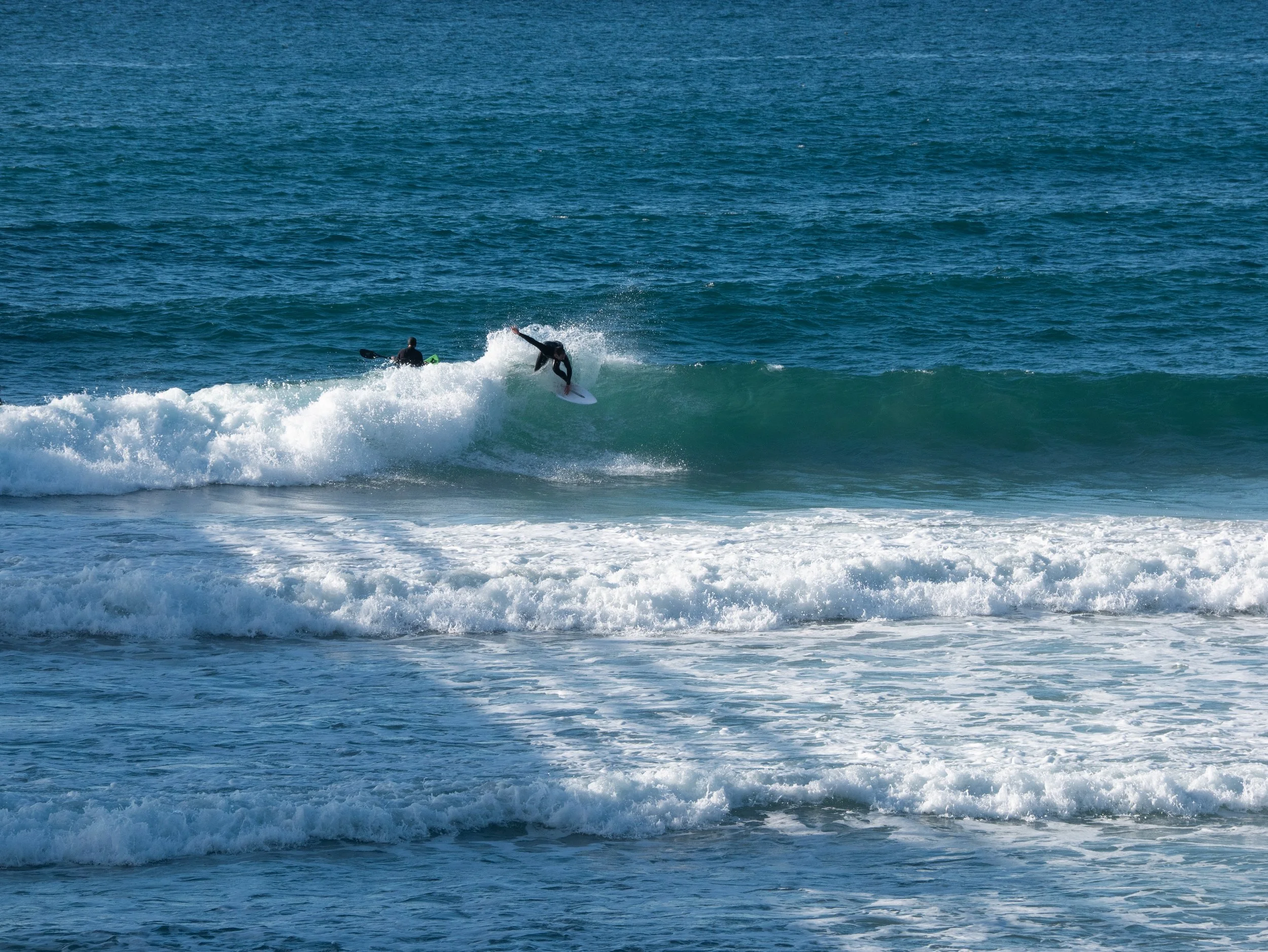 Two surfers riding a wave in the ocean, with one in mid-air and the other paddling.