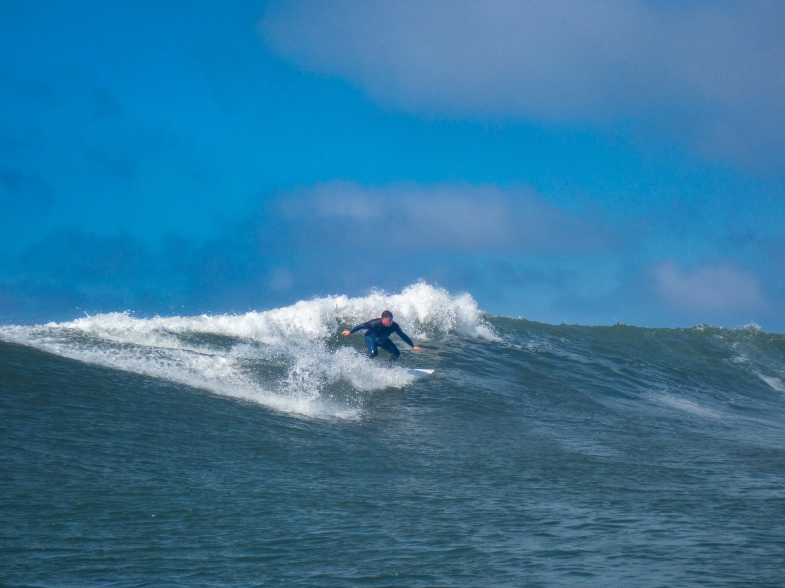 A person surfing on a wave in the ocean under a blue sky.