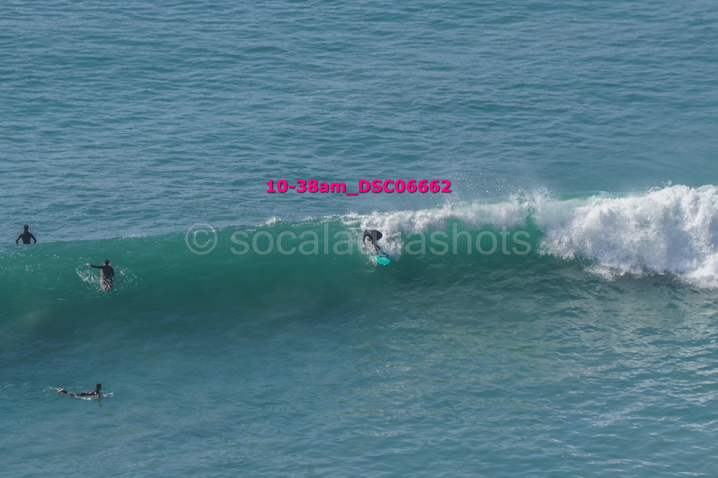 Surfers riding a large wave in the ocean, with some surfers in the water waiting for waves.