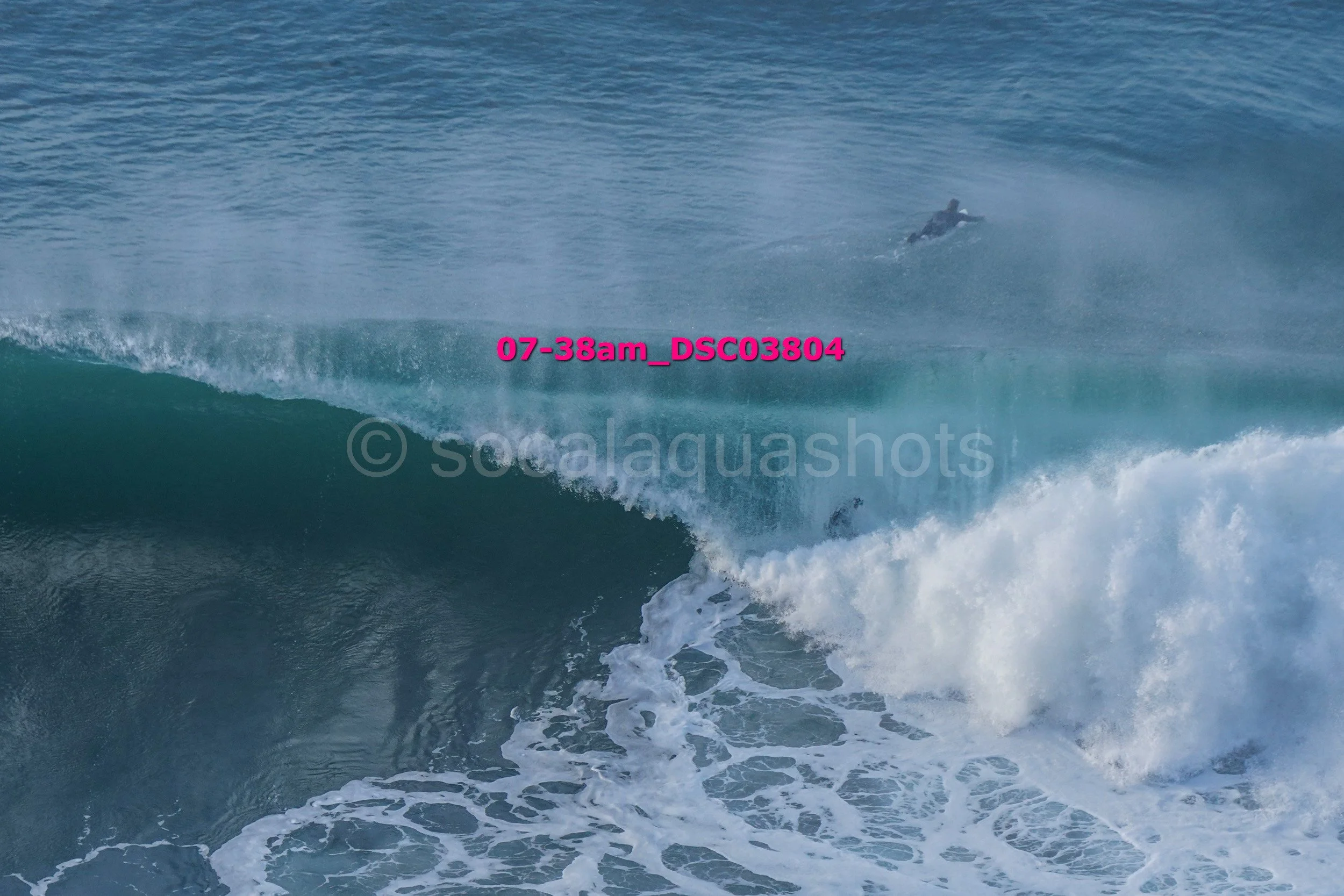 A surfer riding a large wave in the ocean, with another surfer visible in the background.