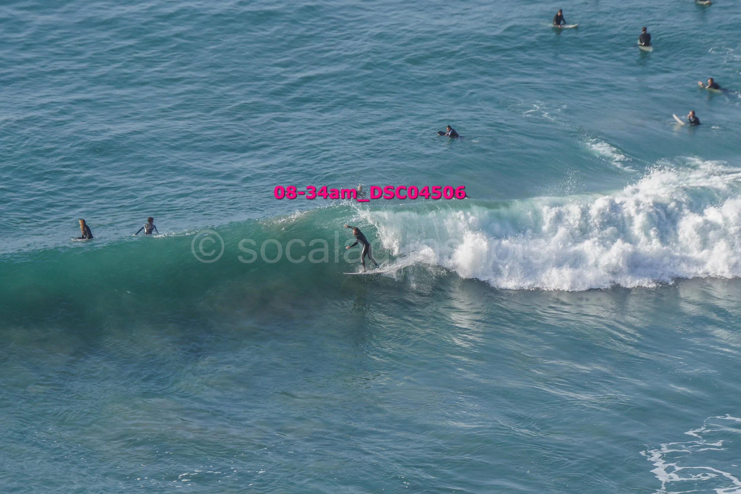 Person surfing on a wave while other surfers watch in the ocean.