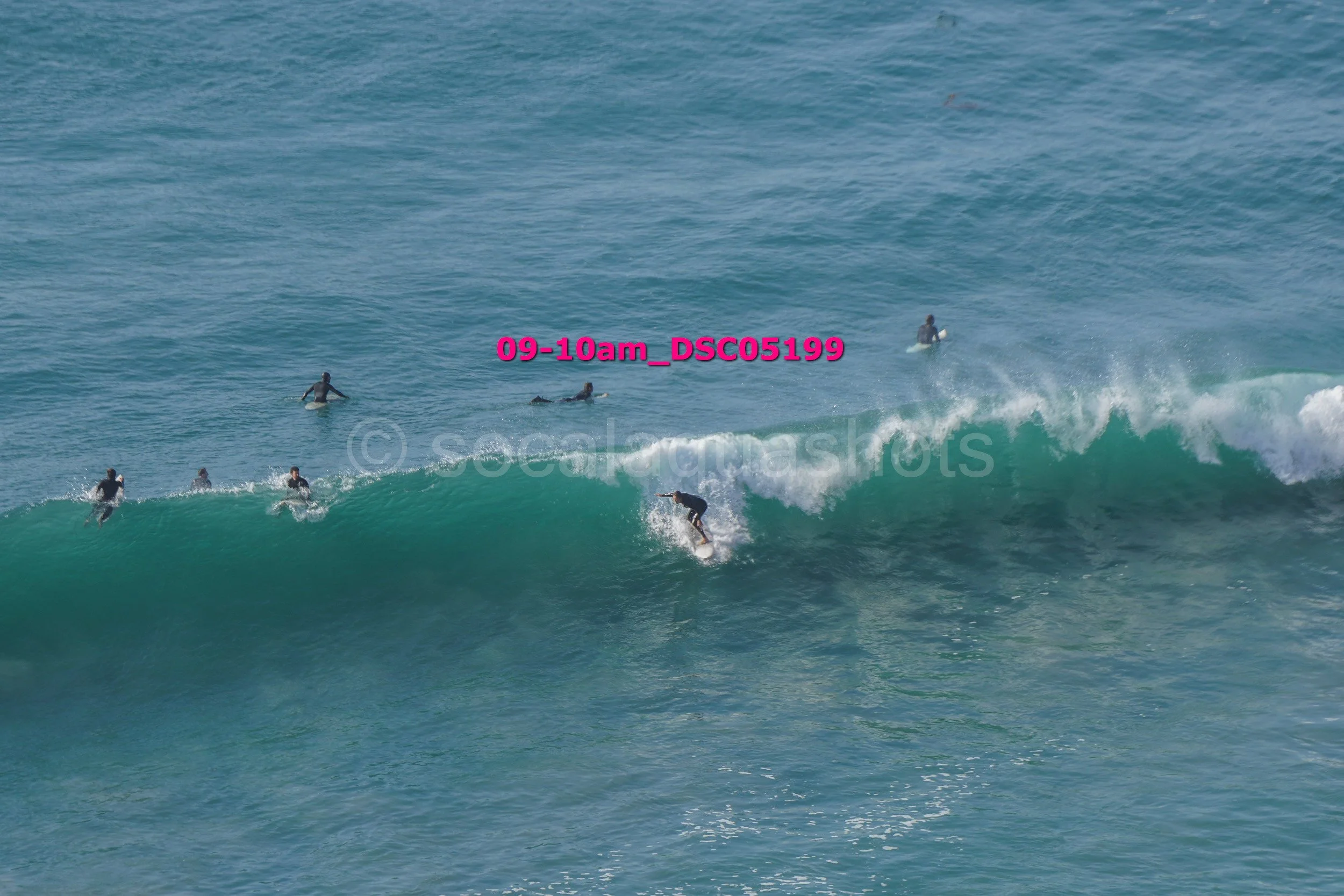 Surfer riding a wave with several other surfers waiting in the water.