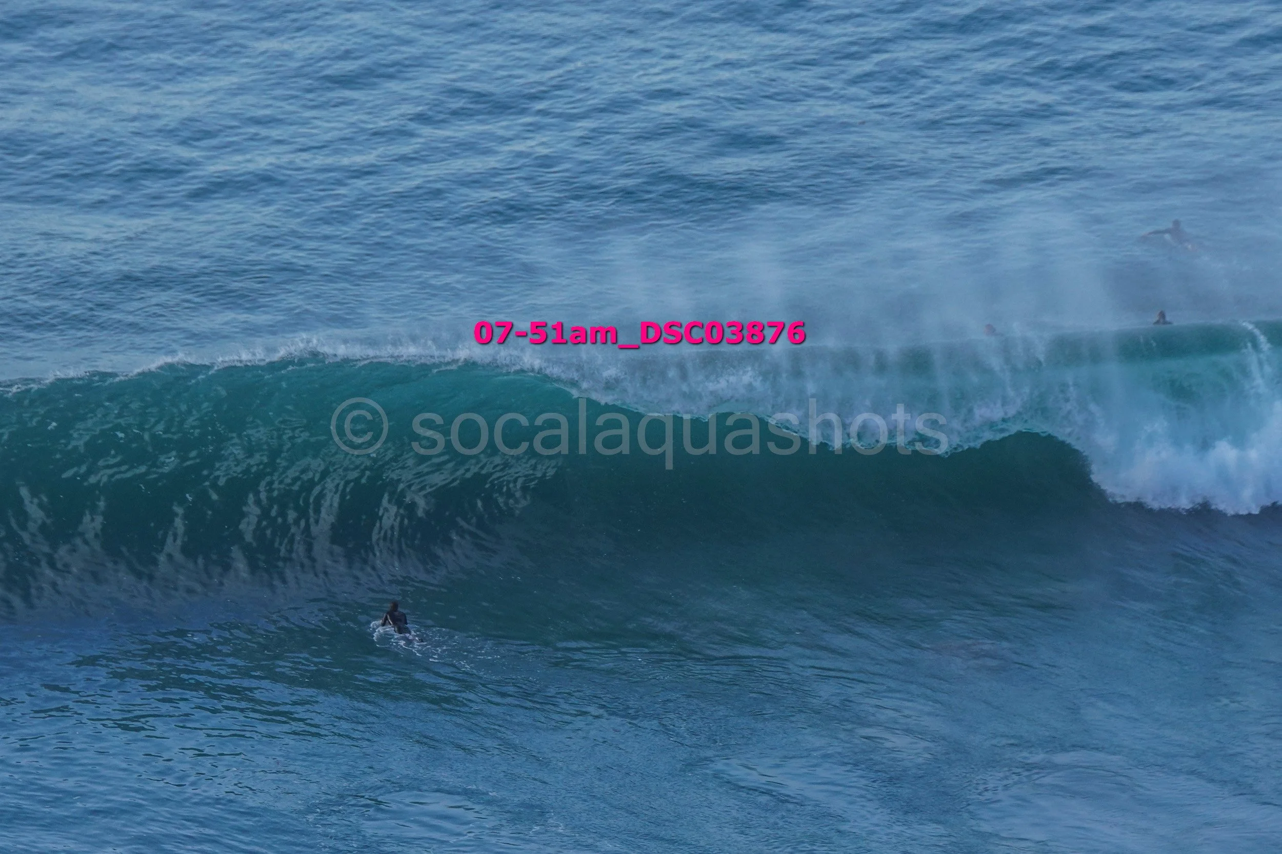 A large ocean wave with surfers riding it, as viewed from the water.