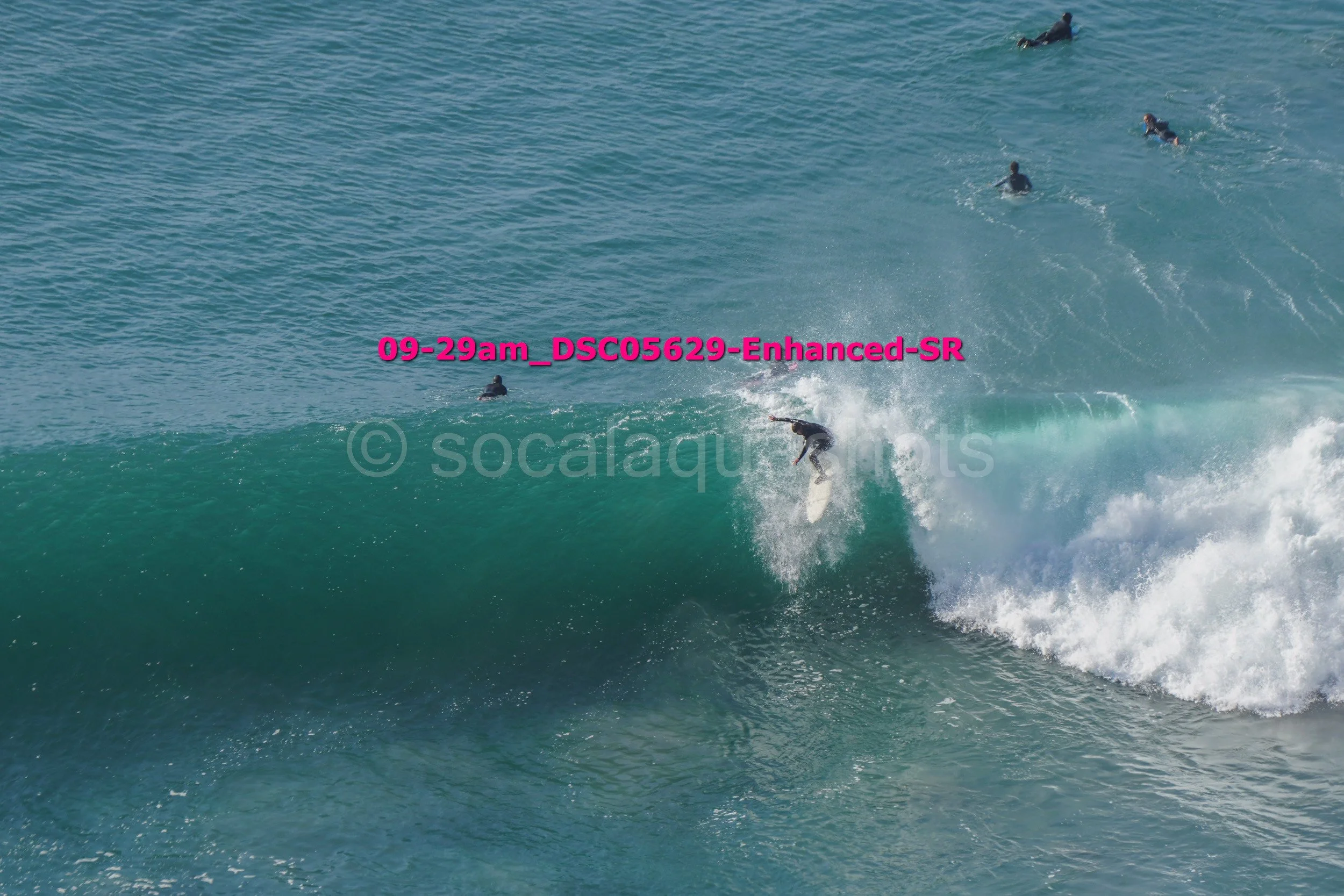 Surfer riding a large wave with several people swimming in the background.