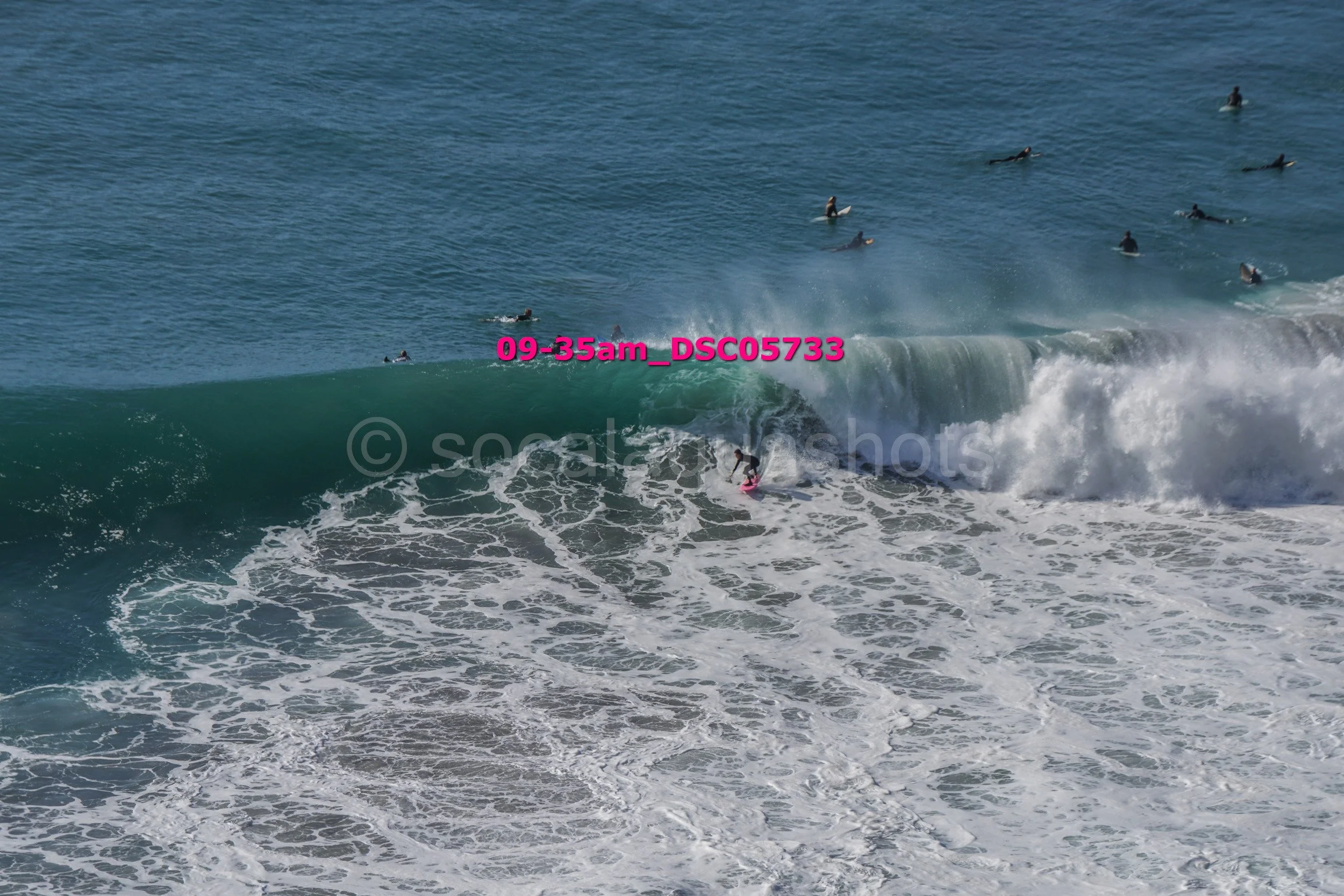 Surfer riding a wave at the beach with other surfers in the ocean.