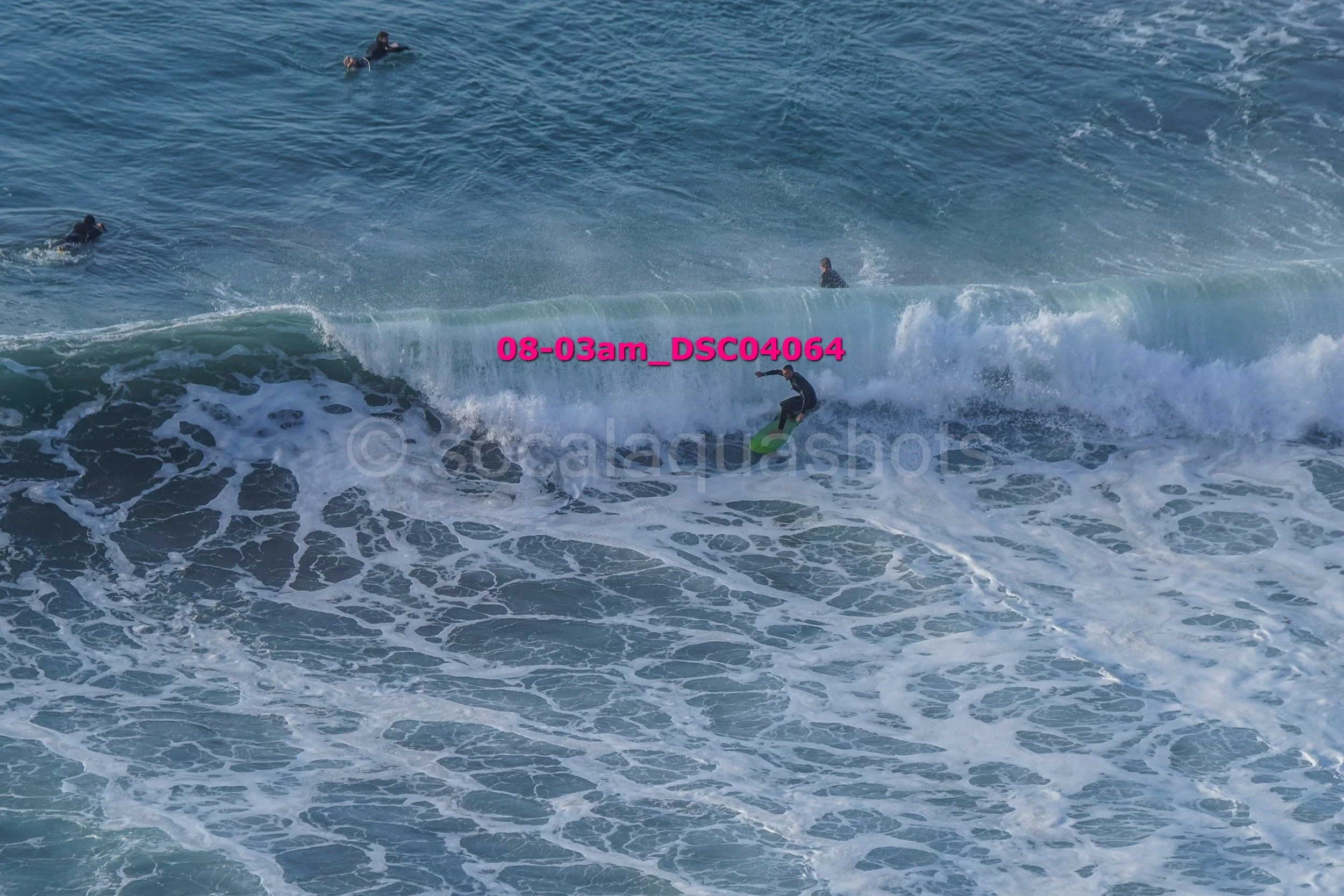A person surfing on a wave in the ocean, with three other surfers visible in the water nearby.