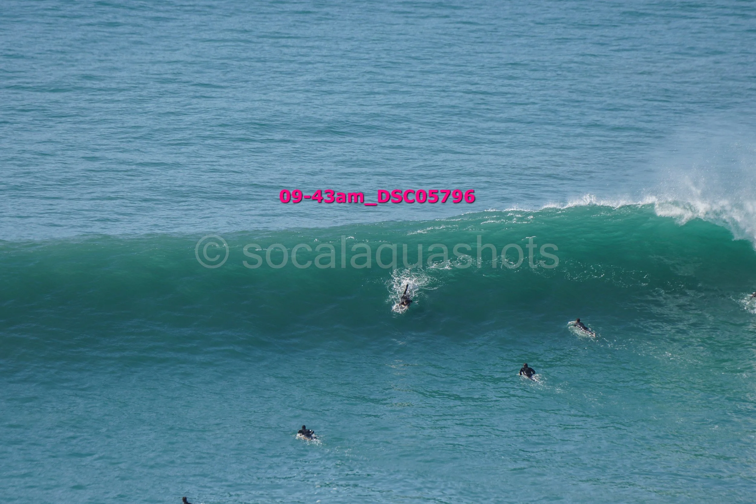 Surfers riding a large wave in the ocean with the sun shining.
