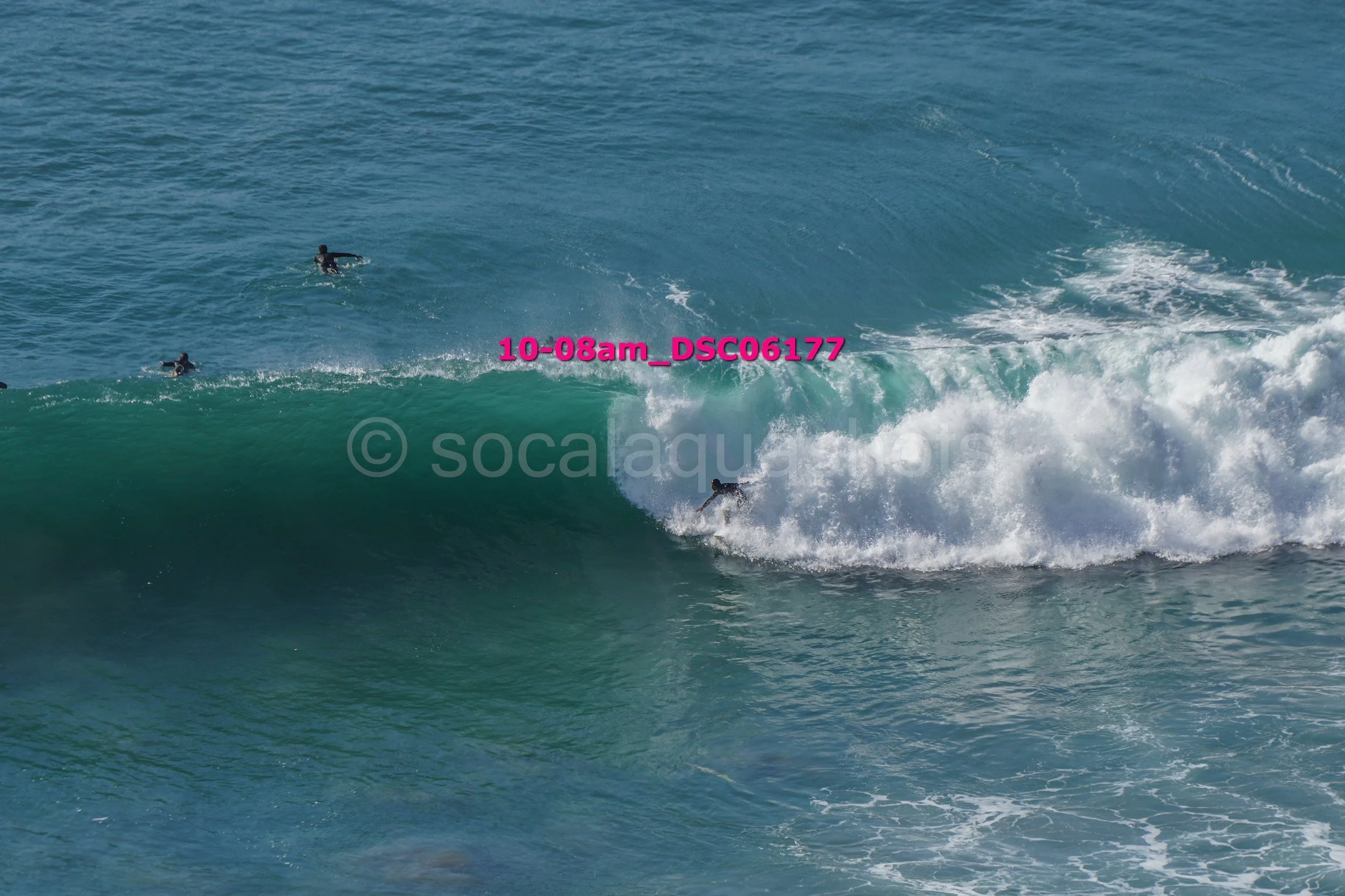 Surfer riding a large wave with three other surfers in the water nearby.