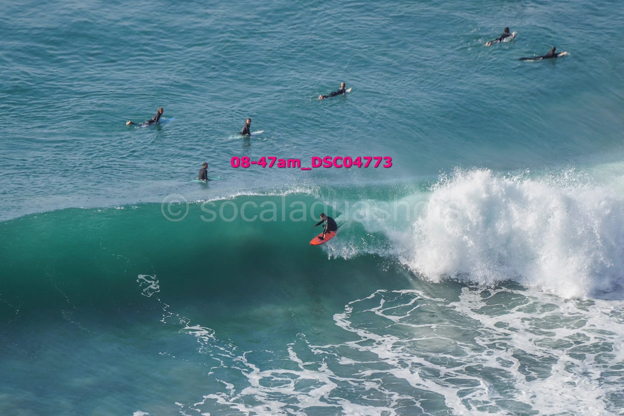 A surfer riding a wave with a group of surfers in the water watching from behind.