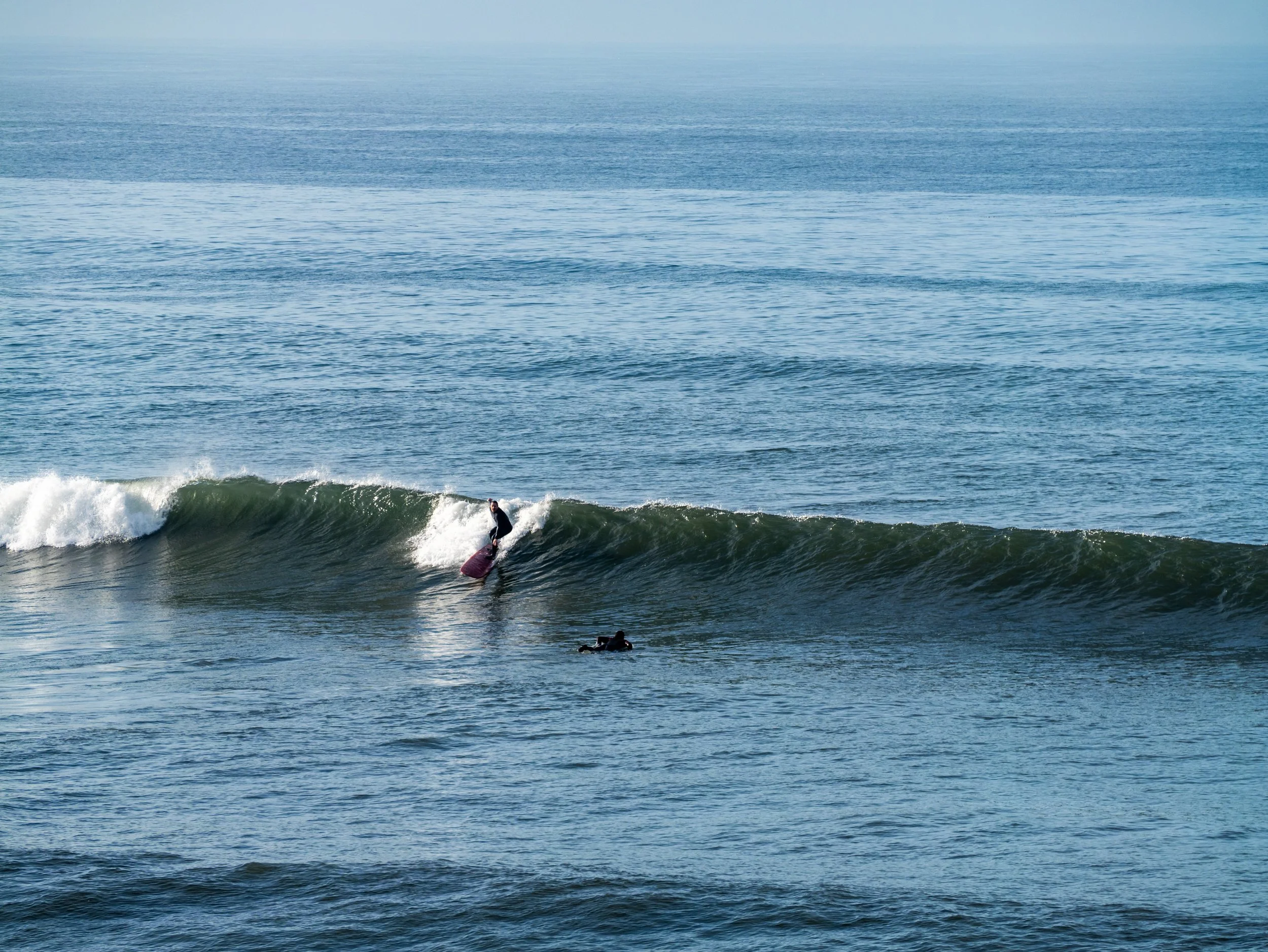 A person surfing on a wave in the ocean with a photographer or another person in the water nearby.