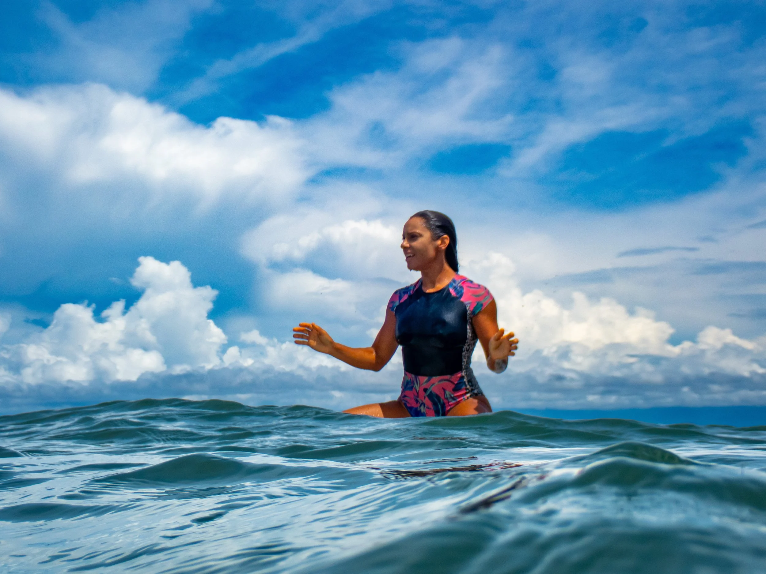 Woman in a colorful swimsuit standing in the ocean under a partly cloudy sky.