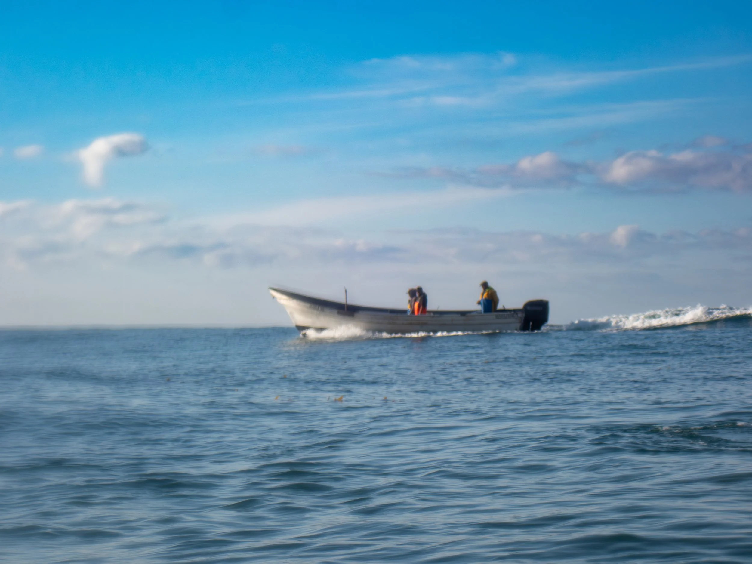 A boat with a few people on board cruising on the ocean under a partly cloudy sky.
