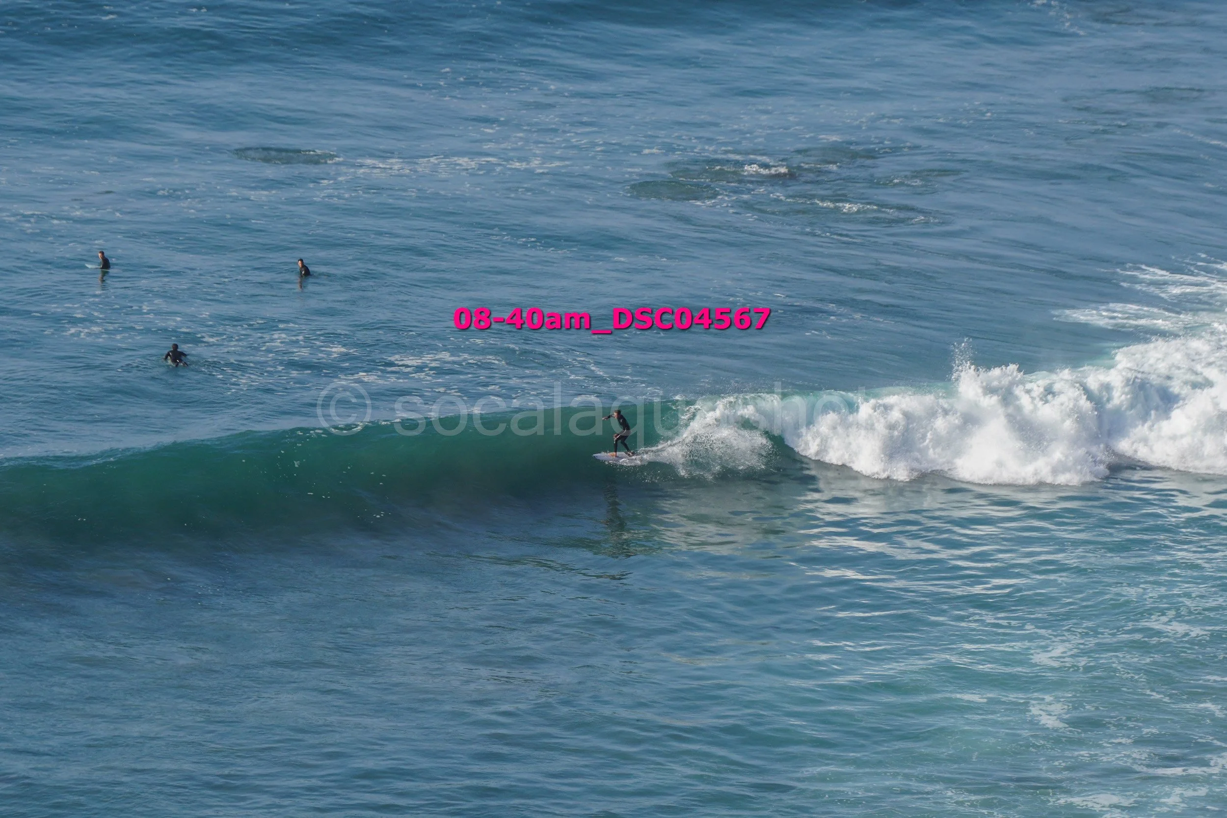 A person surfing on a wave in the ocean with four other surfers in the water nearby.
