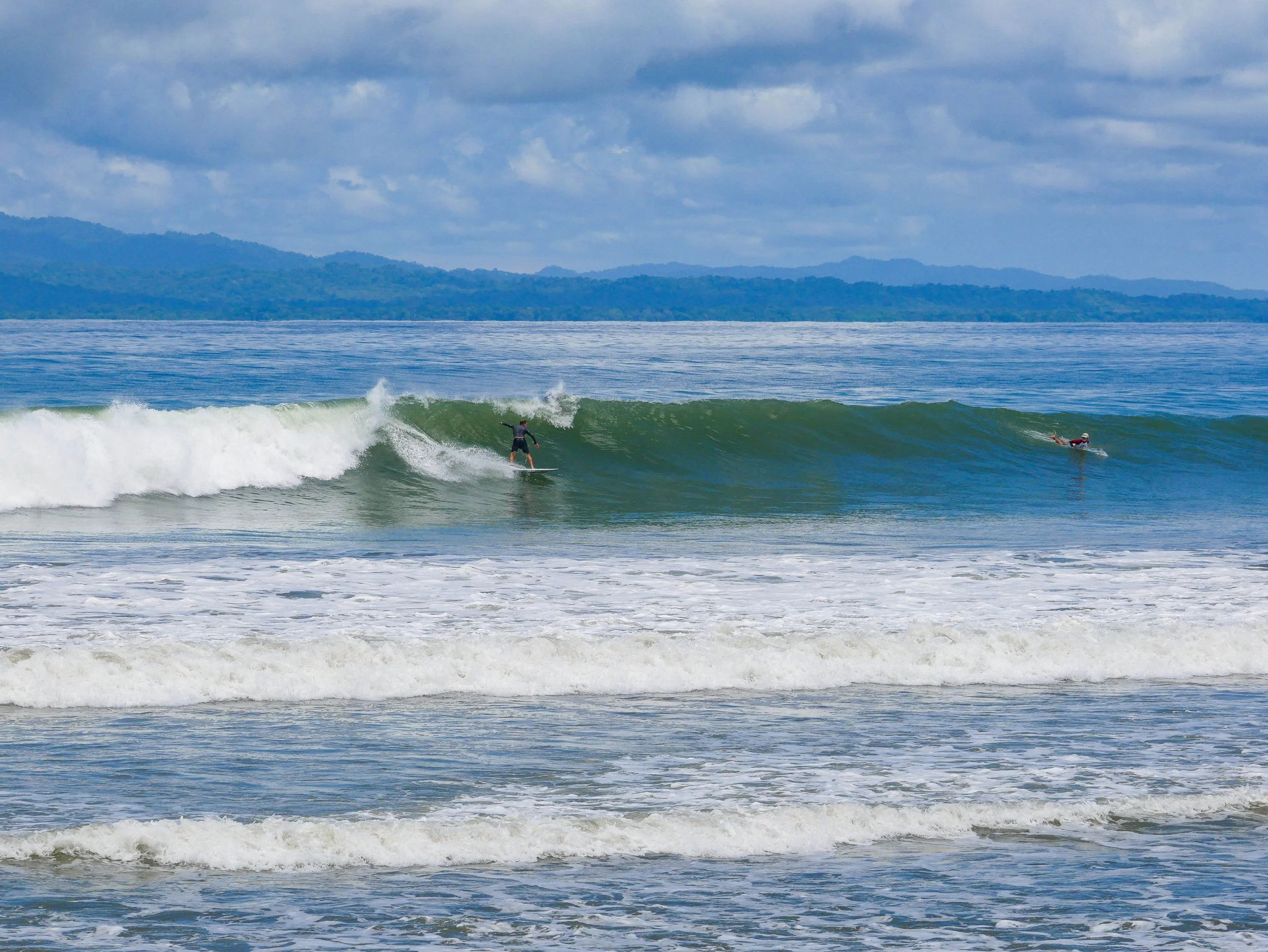 Surfers riding waves on a sunny beach with mountains in the background